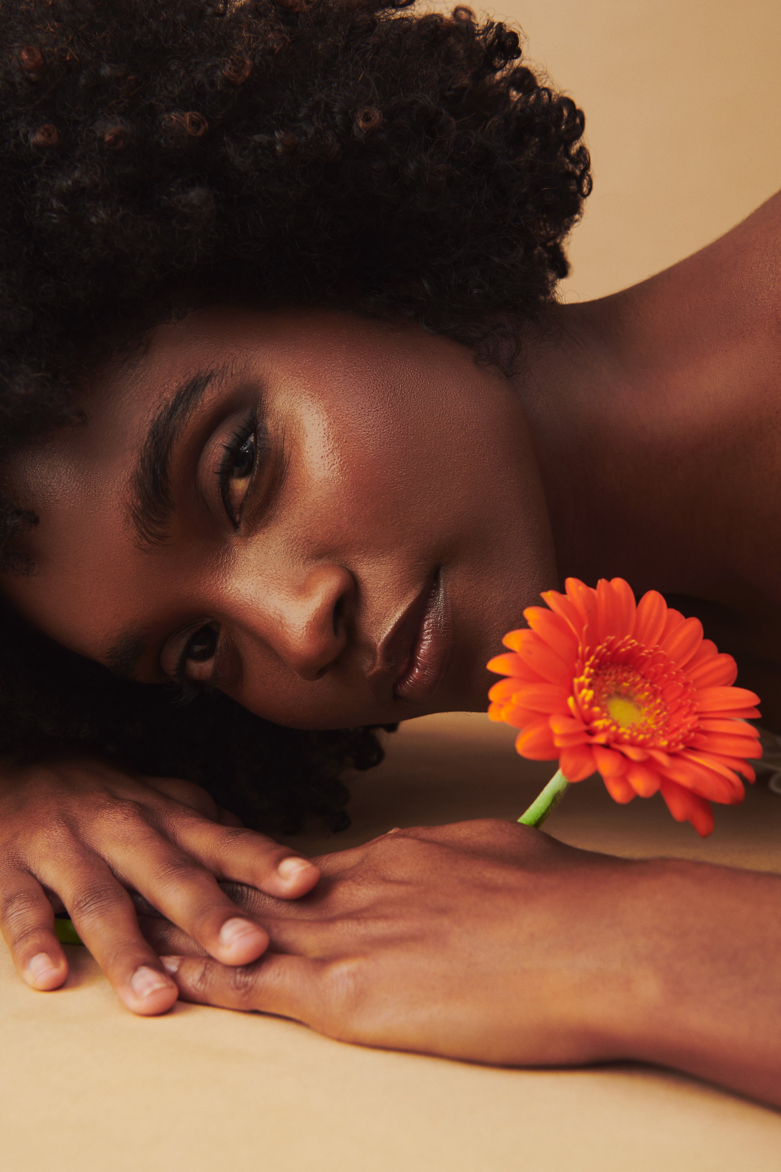 Commercial product photography featuring a model with an orange flower shot by QUEST Production Co., London fashion photographers. The model is posed against a beige background.