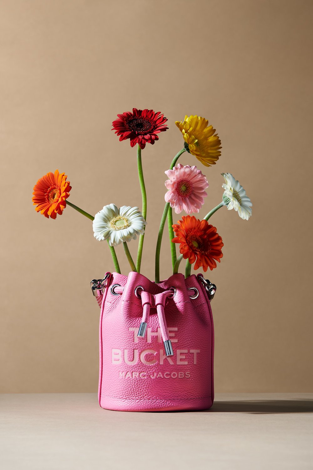 Commercial product photography of Marc Jacobs' pink bucket bag with colorful flowers shot by QUEST Production Co., London fashion photographers. The bag is displayed against a beige background.