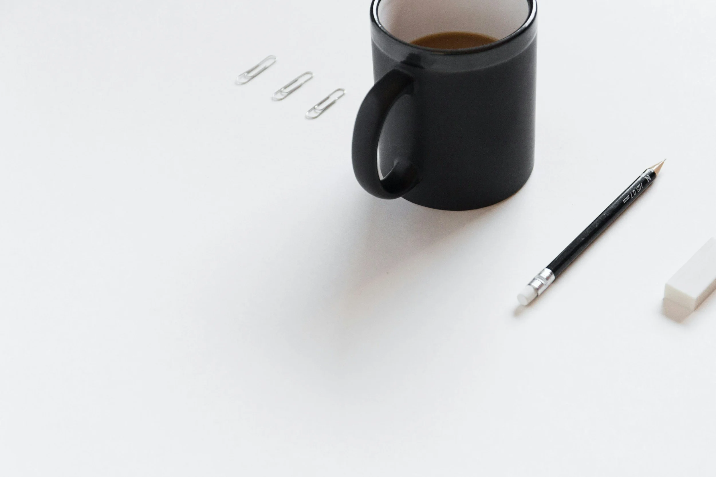 Black coffee mug, pencil, paper clips, and eraser on a white surface.