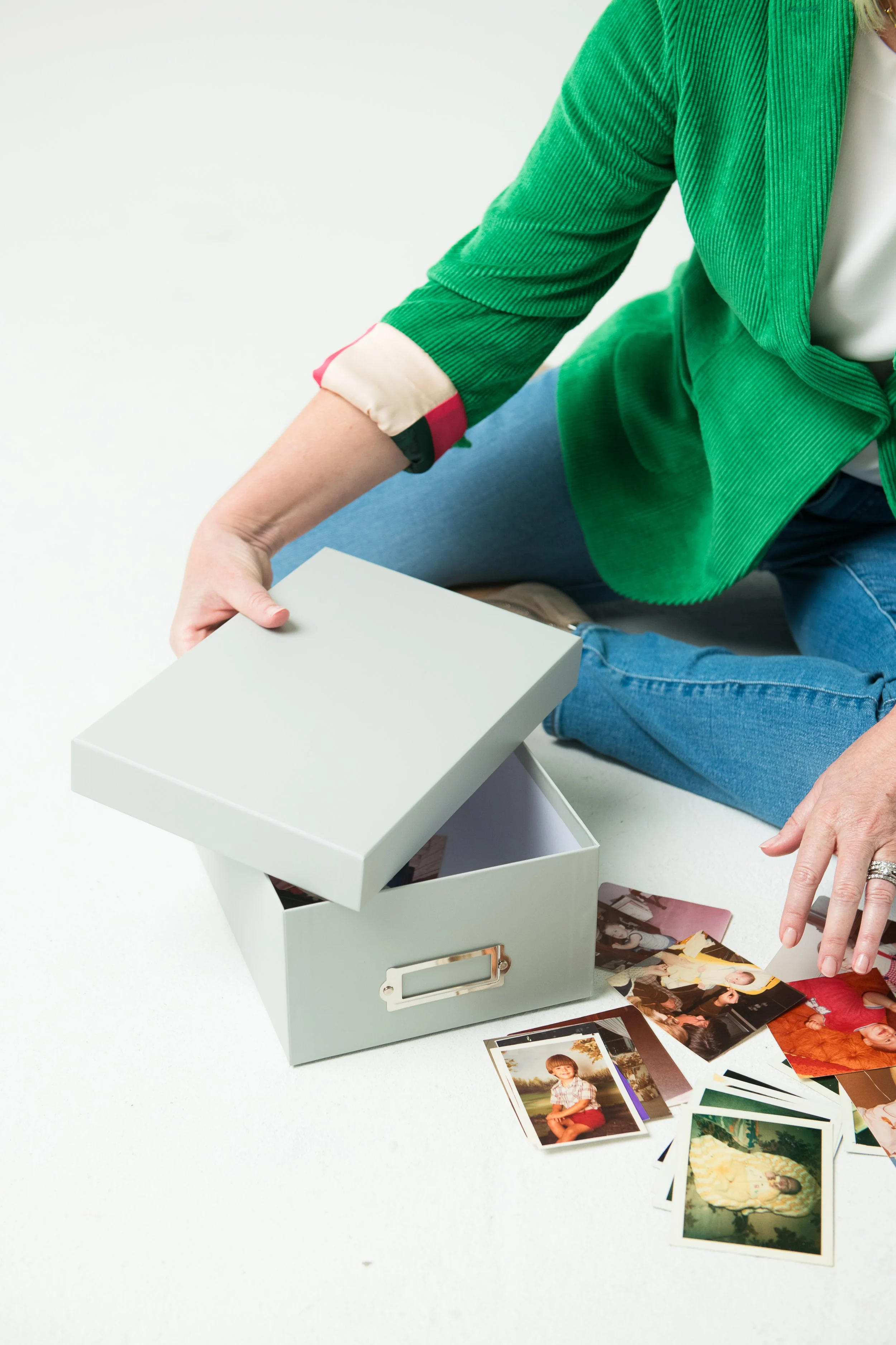 Jennings King wearing a green jacket and jeans sitting on the floor, opening a box filled with old photos scattered around.