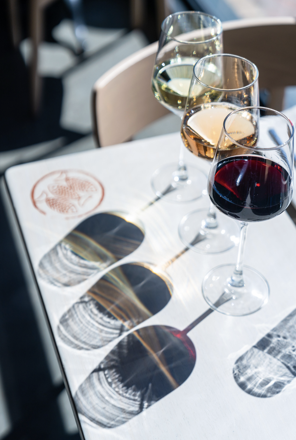 Three glasses of white wine, rosé, and red wine on a white tablecloth, casting shadows in sunlight.