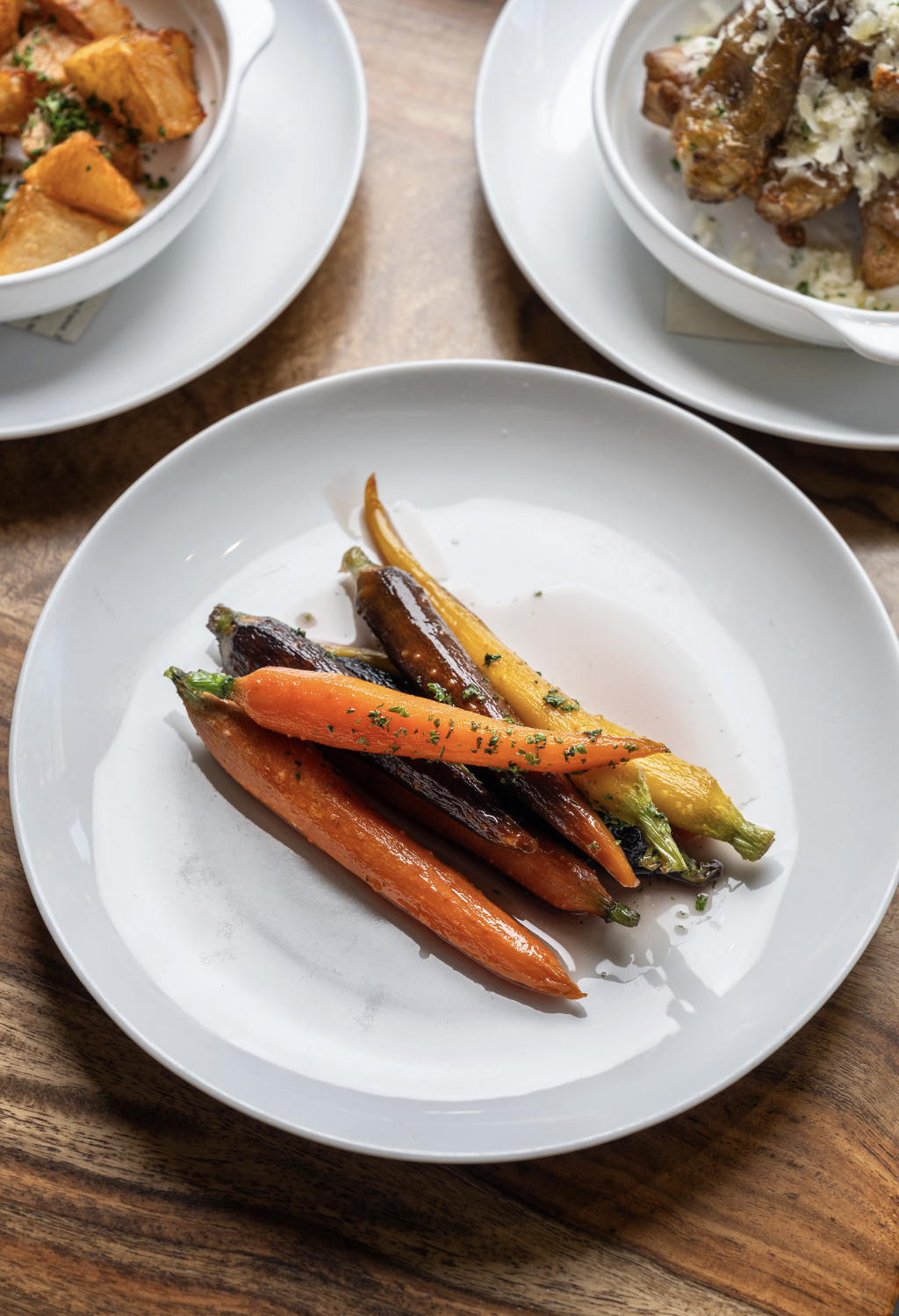 A white plate with roasted baby carrots in various colors, garnished with herbs, on a wooden table.