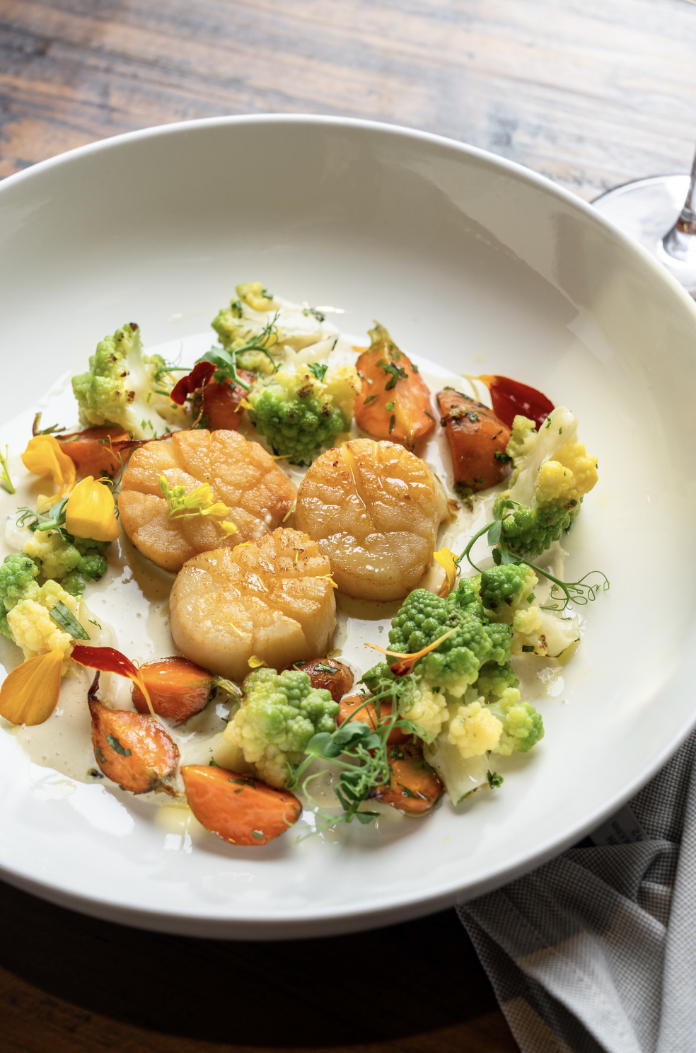 Seafood dish with scallops, roasted vegetables, and microgreens on a white plate.