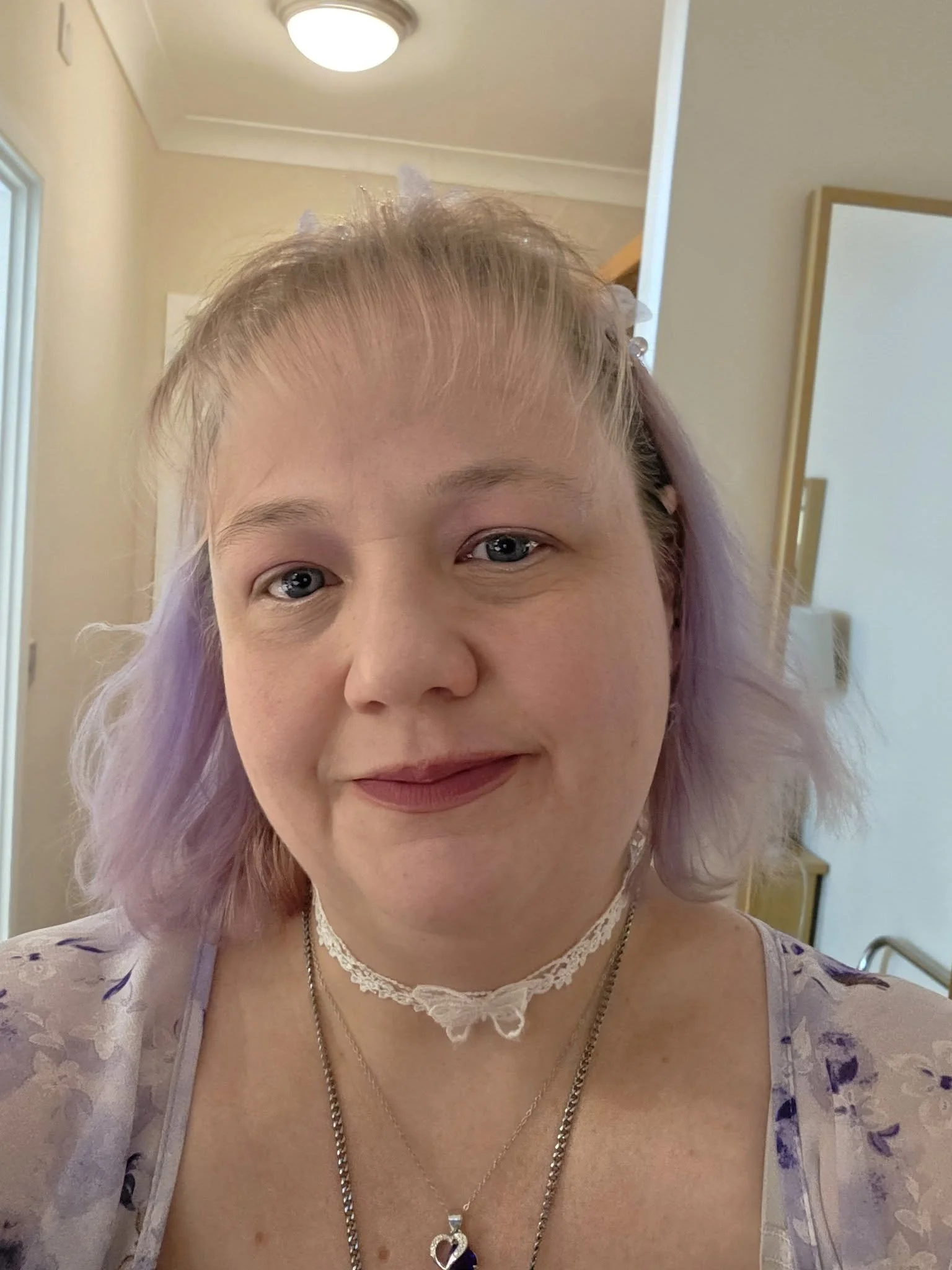 Selfie of Donna Morfett, with purple hair, curled, blonde fringe, wearing light make up and a white butterfly choker