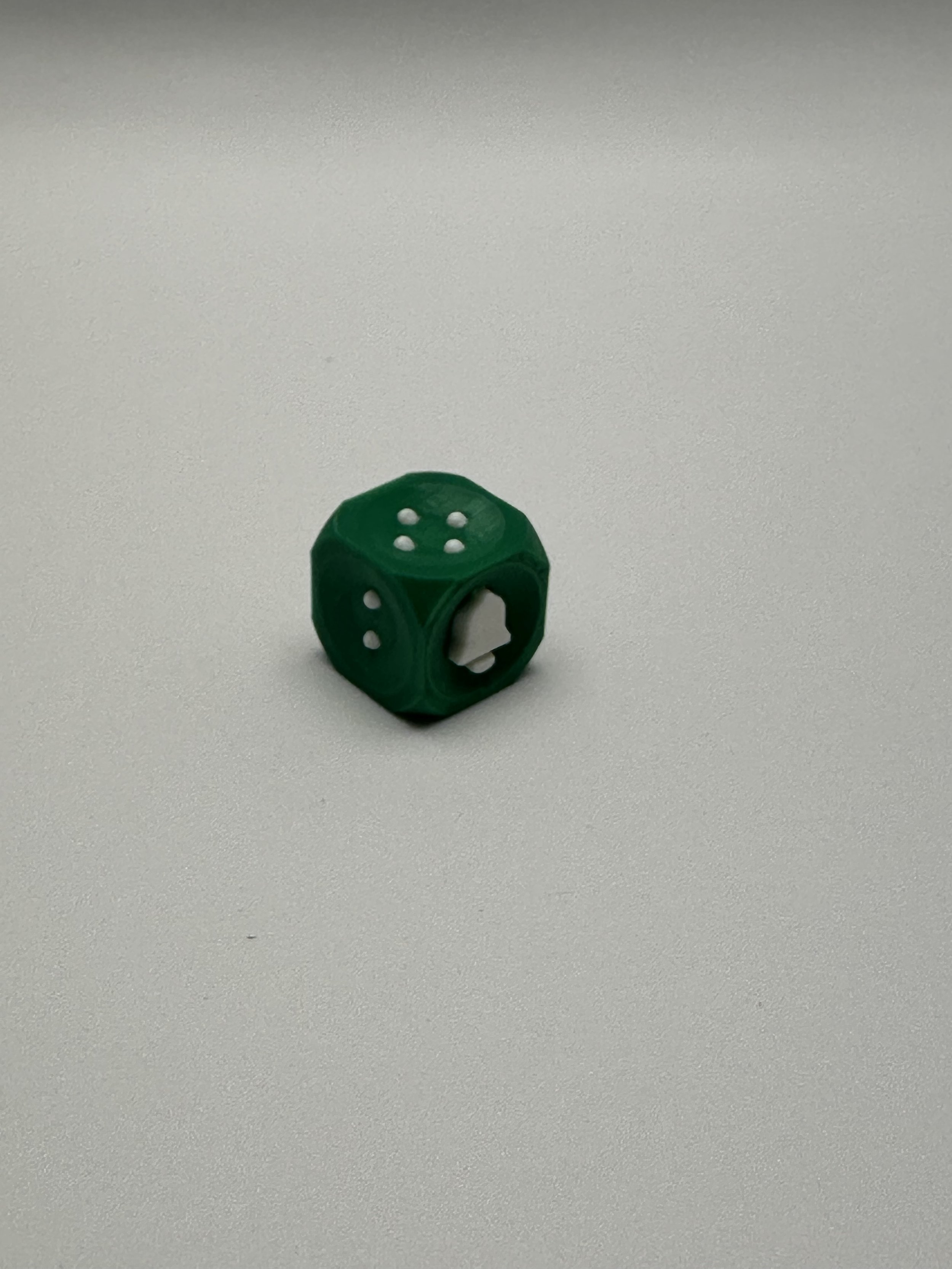 1 green bell die, showing sides 2, 4, and 6(bell) in white.