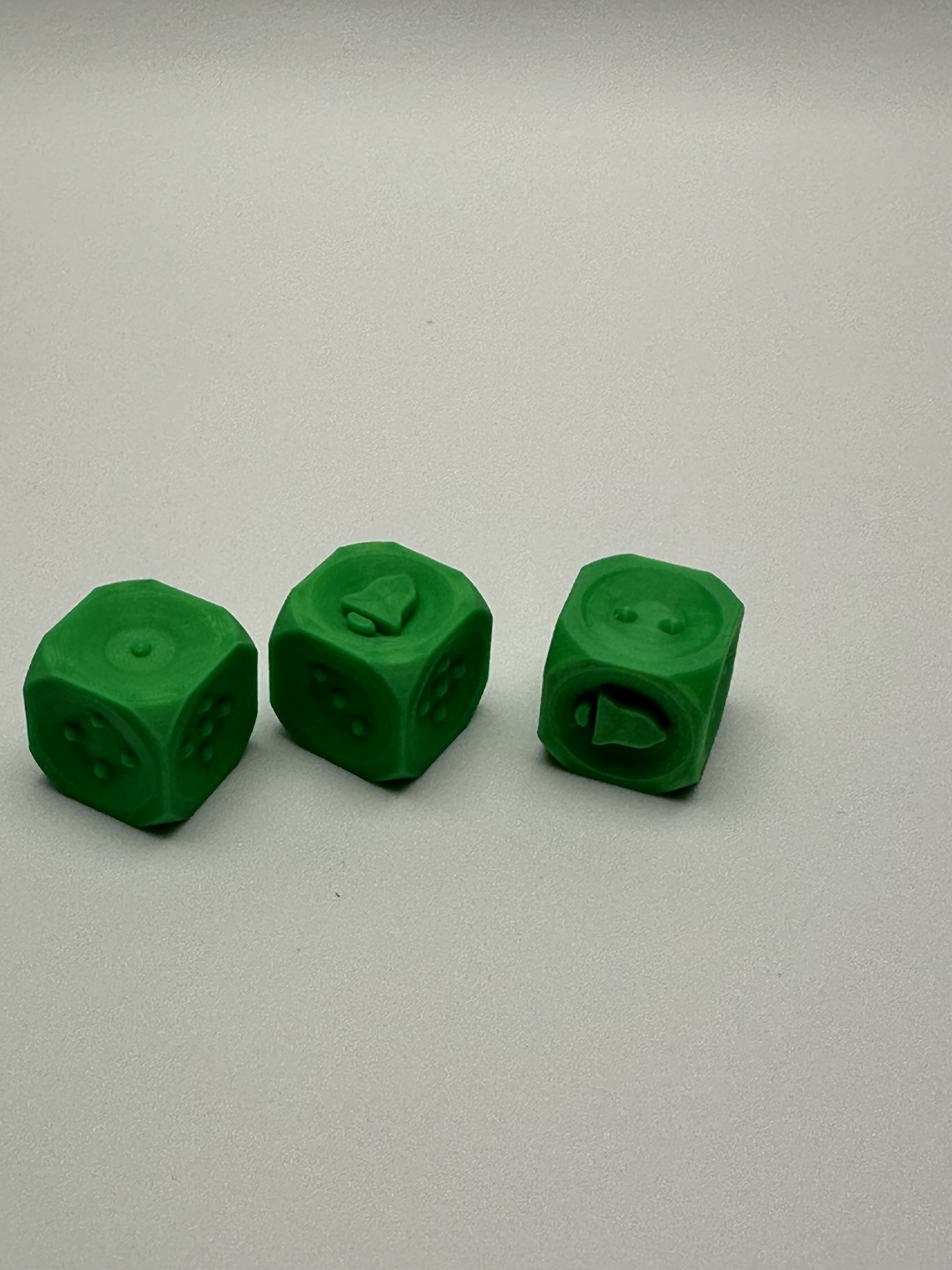 3 green bell dice against a white background, showing sides 1, 6 (bell), and 2.