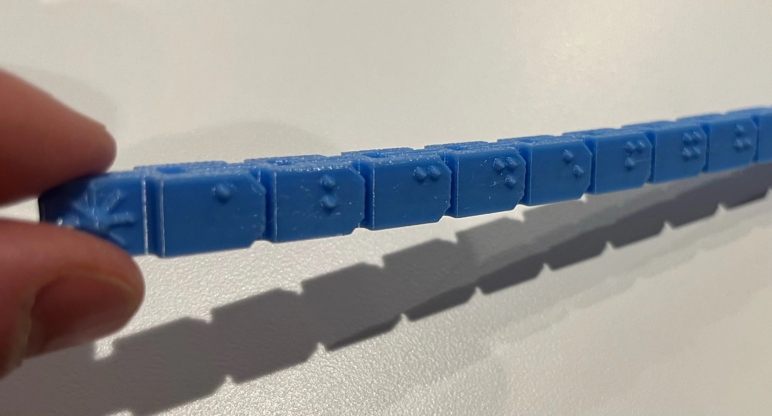 Sky blue fidget configured in a straight line, braille character side showing.
