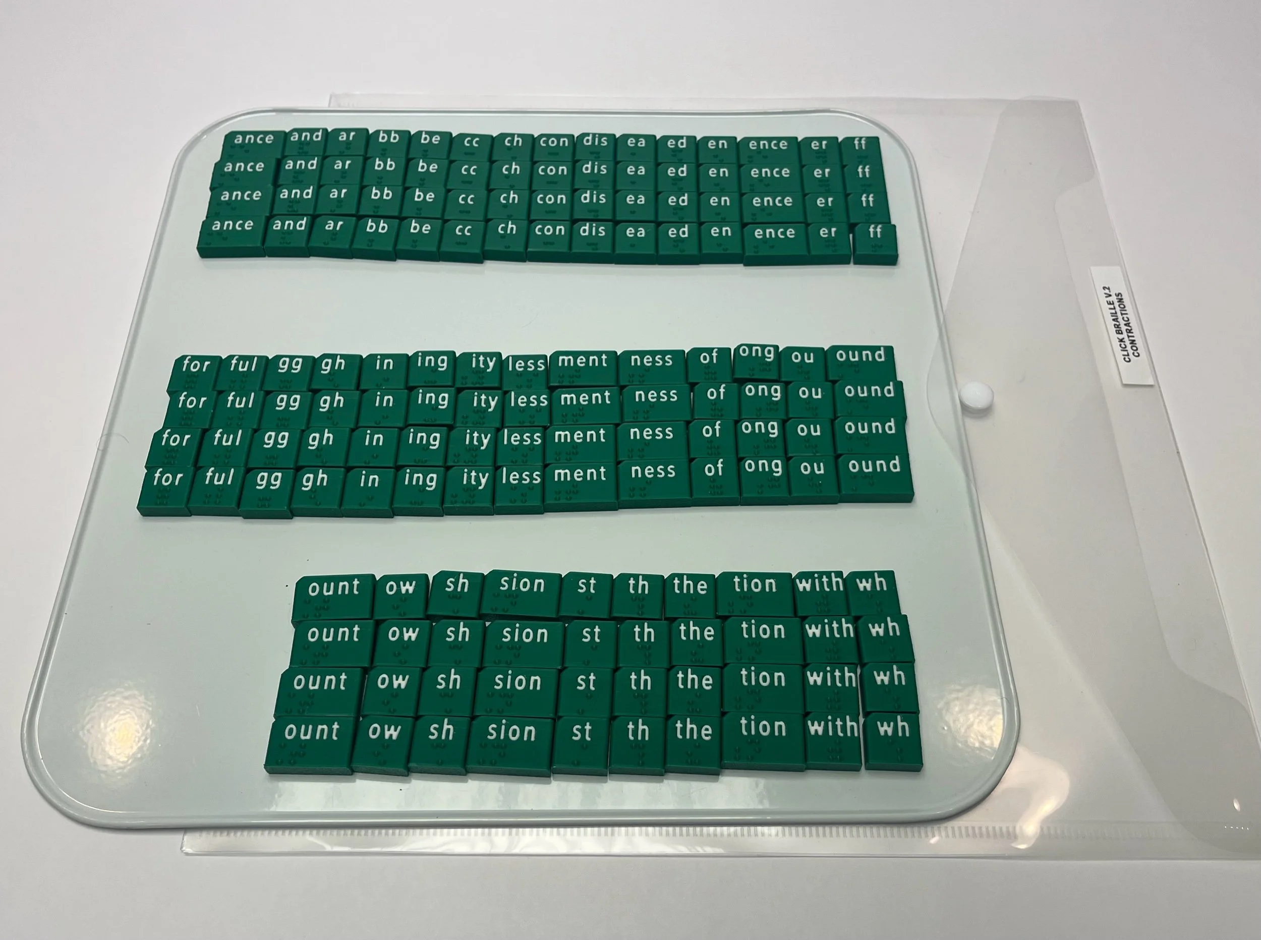 4 of each braille contraction tile (parts of words) shown on an organization board. Tiles are green with white print above the braille.