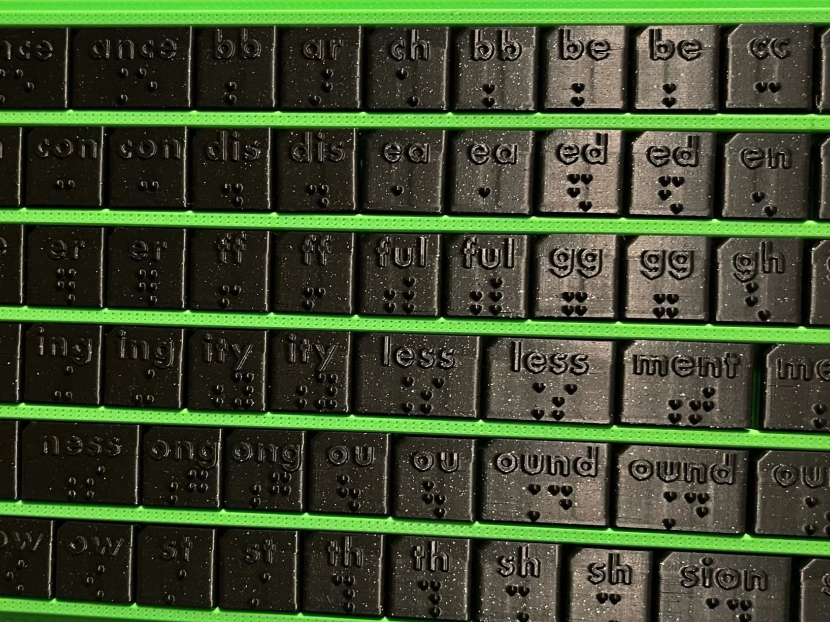 Close up of black braille tiles on a green slide board.