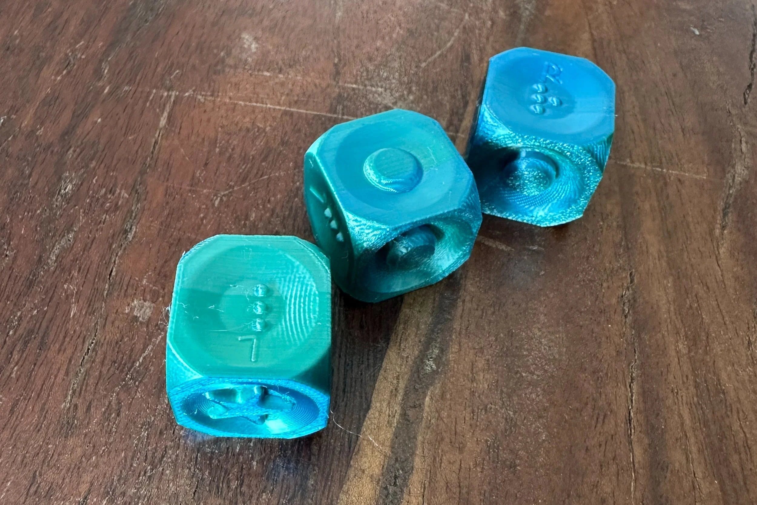 Close-up of 3 shiny blue dice, showing an braille letter "l", circle, and braille letter "r" on the top surfaces.