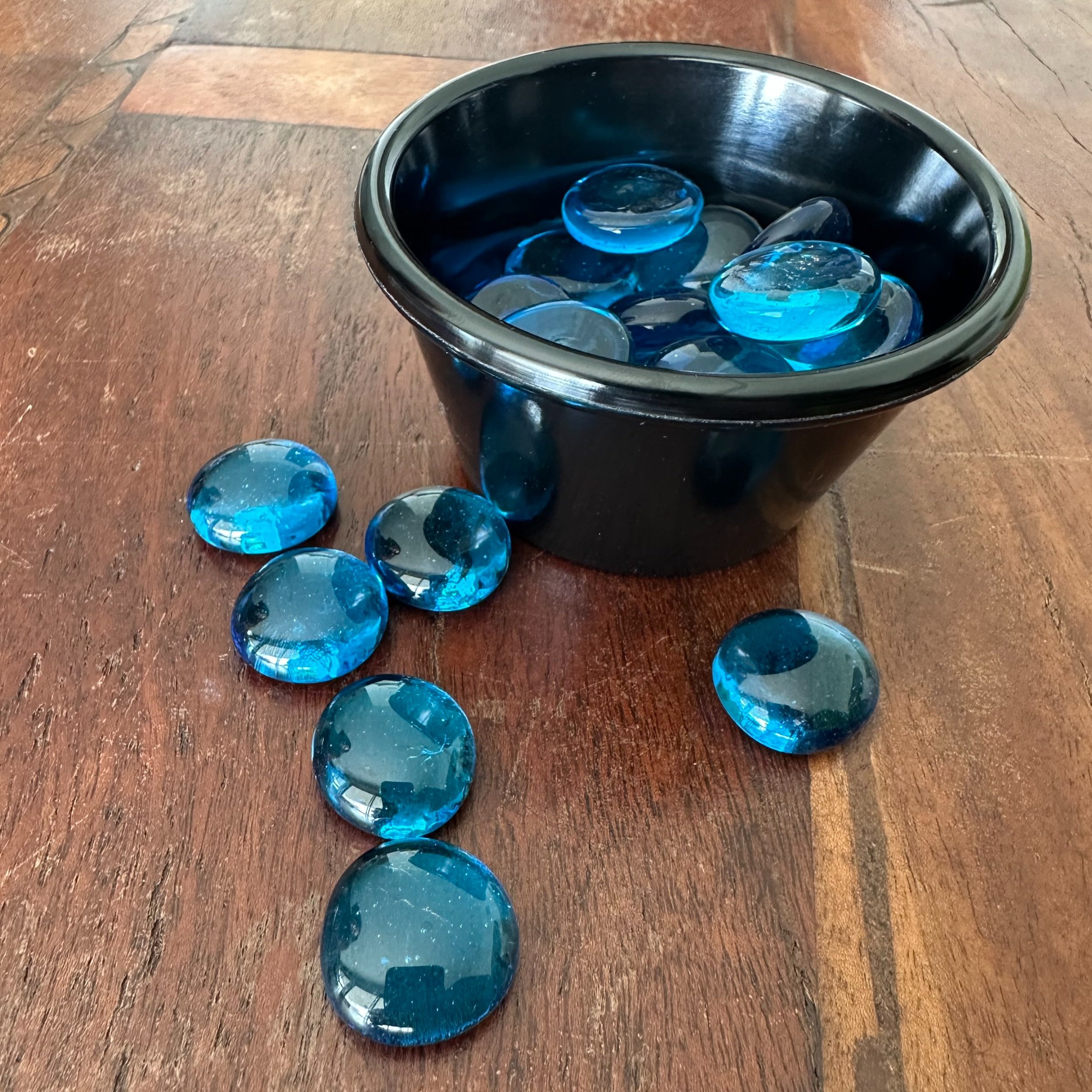 Blue glass bubbles shown in and scattered around a circular cup, against a dark wood table.