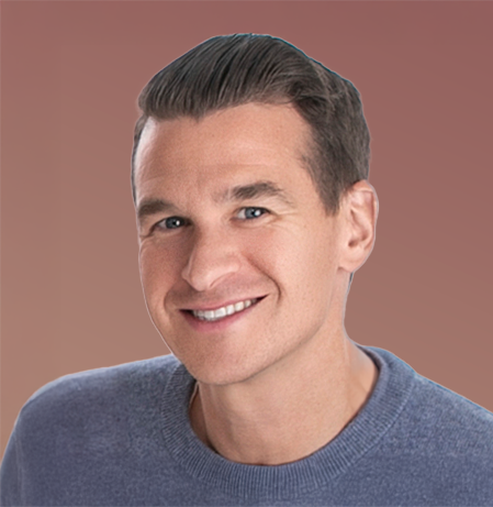 Portrait of a young man with short brown hair, smiling, wearing a blue shirt, against a plain background.