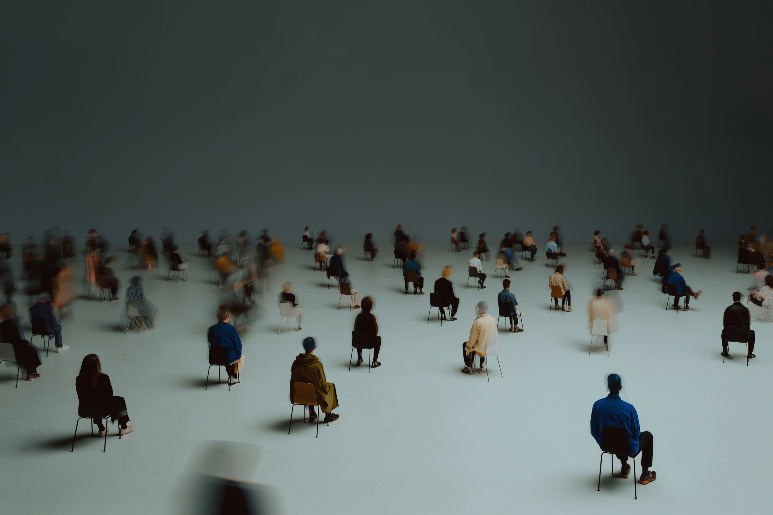 Une salle avec de nombreuses personnes assises sur des chaises espacées, certaines en mouvement, créant un effet de flou.