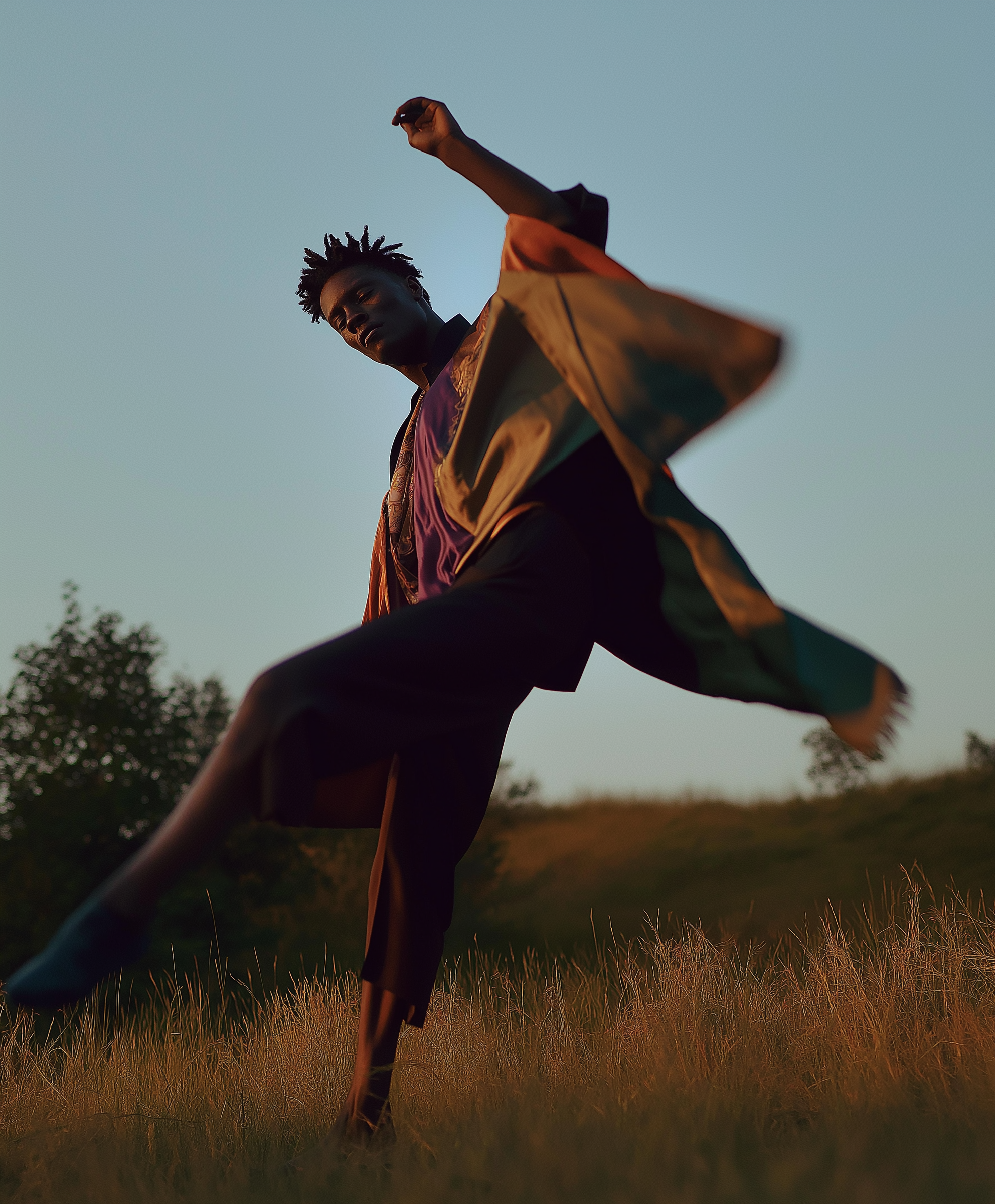 Une personne danse dans un champ lors du coucher de soleil, portant une veste colorée.