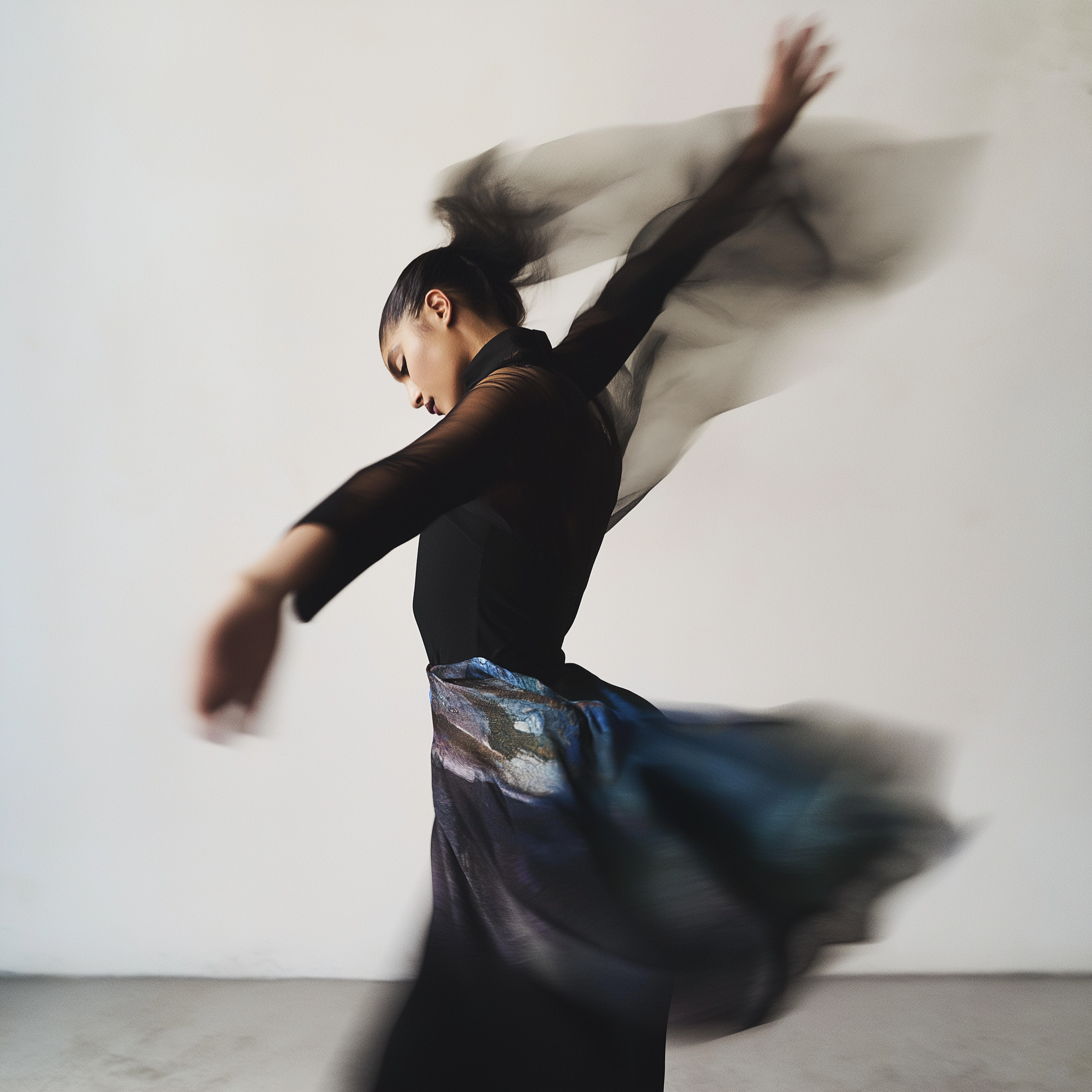 Une femme danse avec un mouvement fluide, portant une robe noire et une jupe colorée, devant un fond blanc