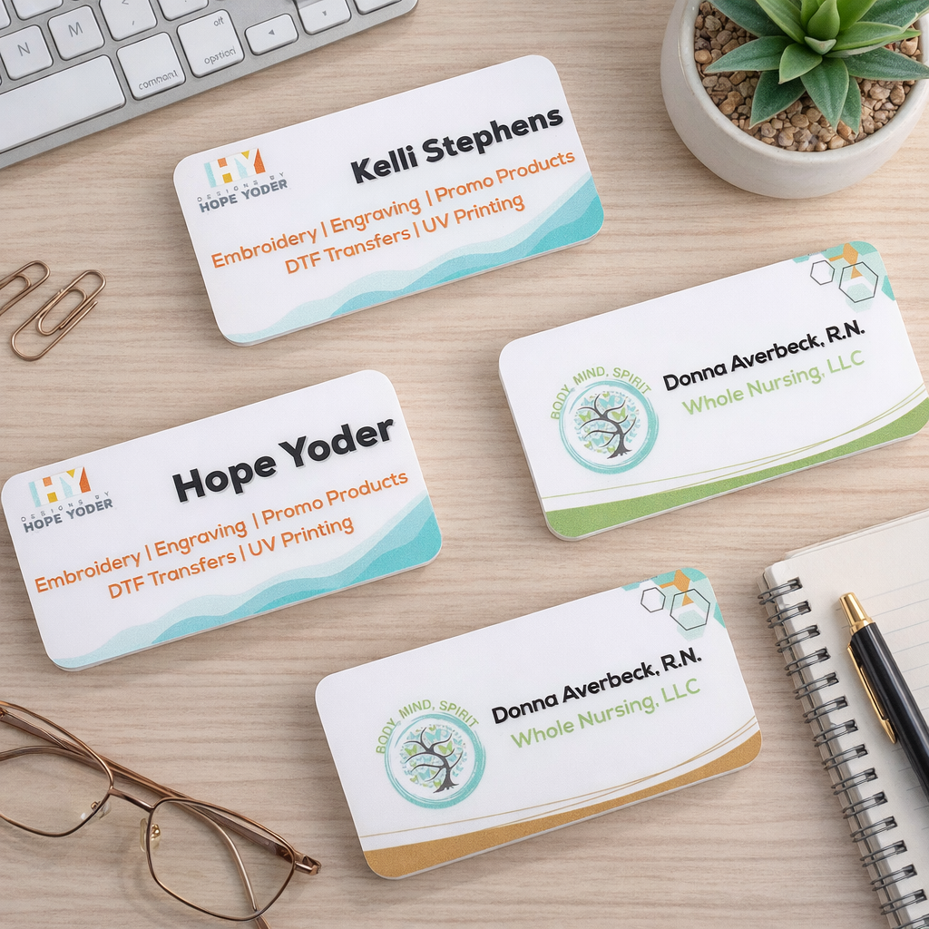 Four business cards on a light wooden desk, two for Kelli Stephens and two for Donna Averbeck, R.N., with a white keyboard, a pair of glasses, a black and gold pen, a small spiral notepad, a gray pot with a green succulent plant, and gold paper clips