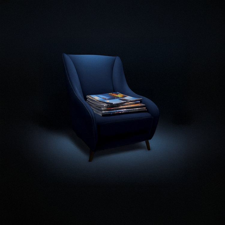 A dark blue armchair with a stack of magazines on it, illuminated by a focused light in a dark setting.