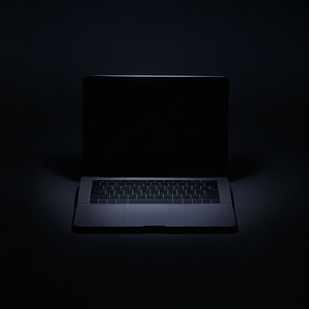 A closed laptop in a dark environment with a faint glow on the edges of the screen and keyboard.