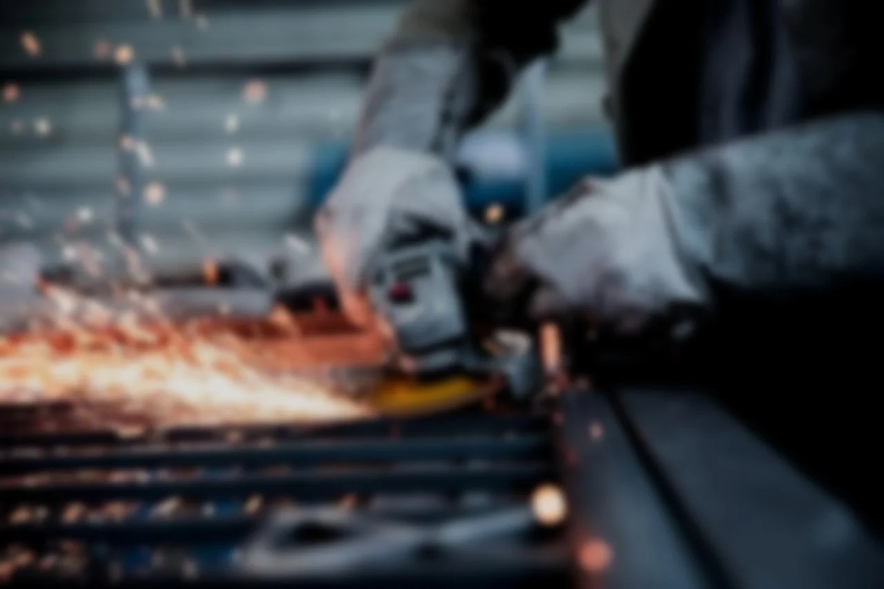Close-up of a welding process on metal, with sparks flying and a worker in protective gear.