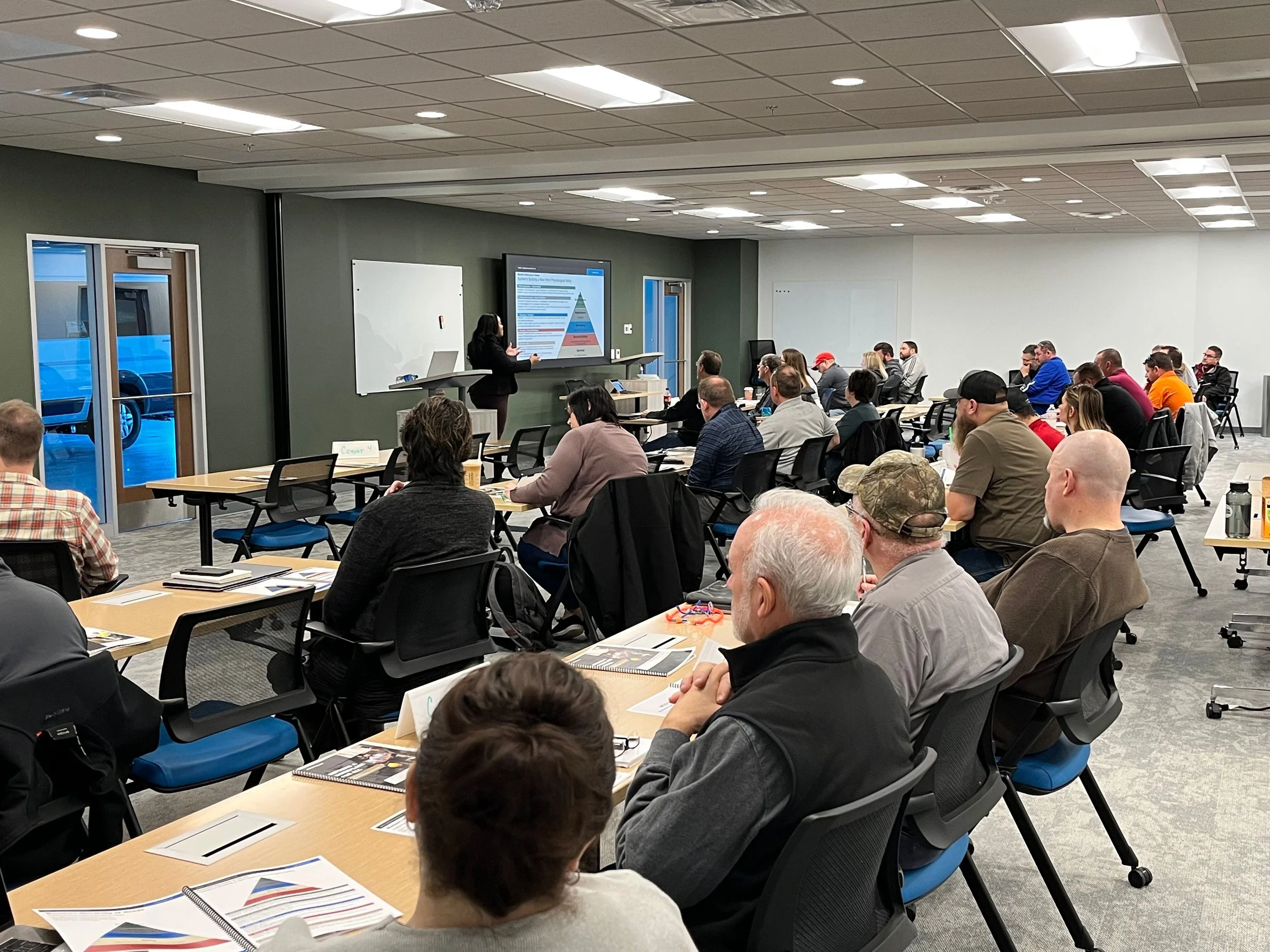 A group of people attending a presentation in a conference room with a woman speaker using a large screen display.