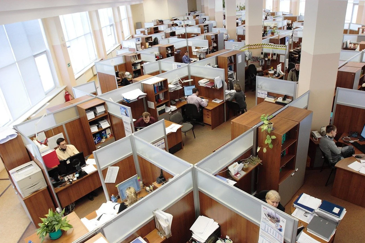Office space with multiple cubicles and employees working at desks, viewed from an elevated angle.