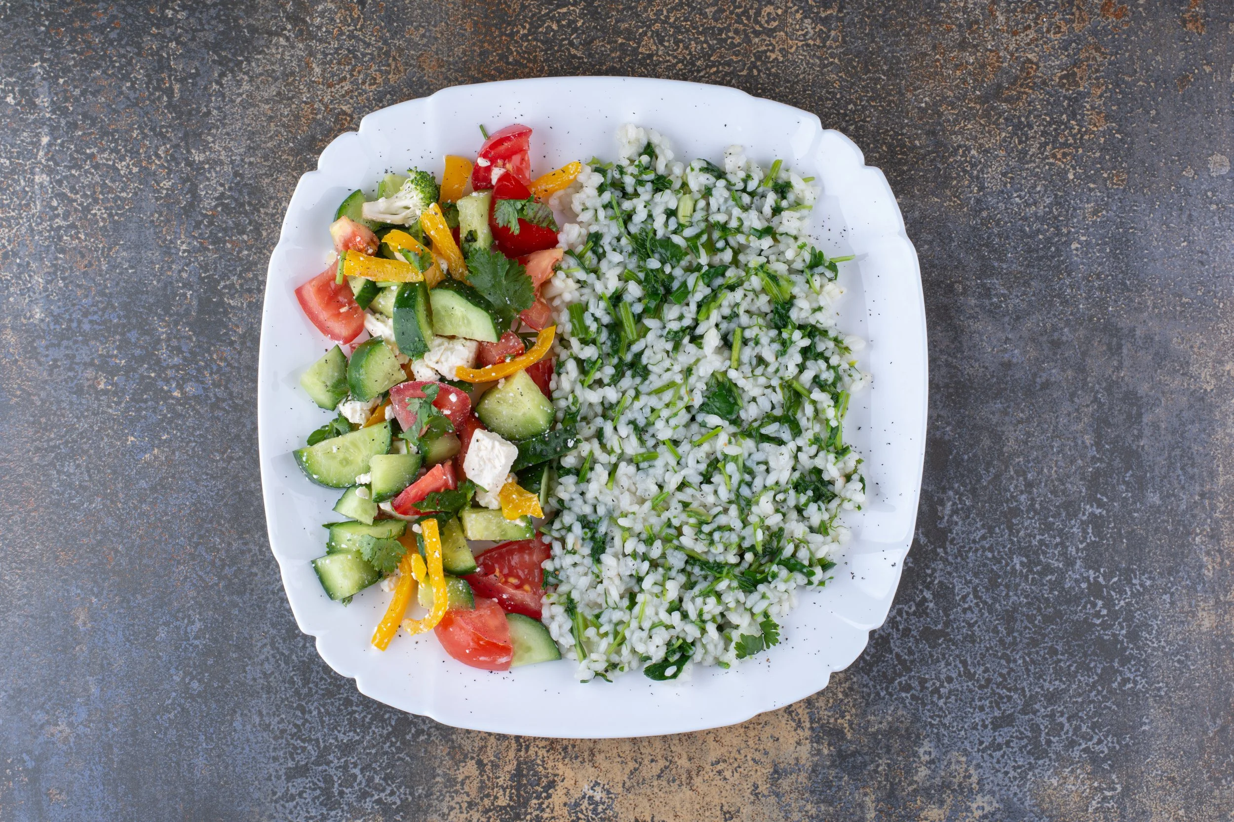 A white plate with a vegetable salad and tabbouleh on a textured gray surface.