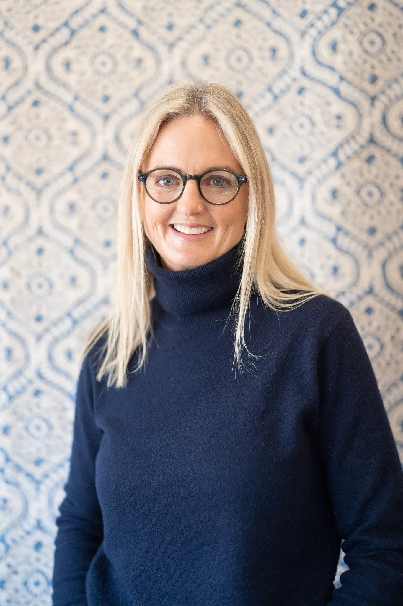 Lisa Dawson, founder of the business, looking directly at the camera against a wall of sample paint and fabric. She is blonde with striking blue eyes and a kind smile. 