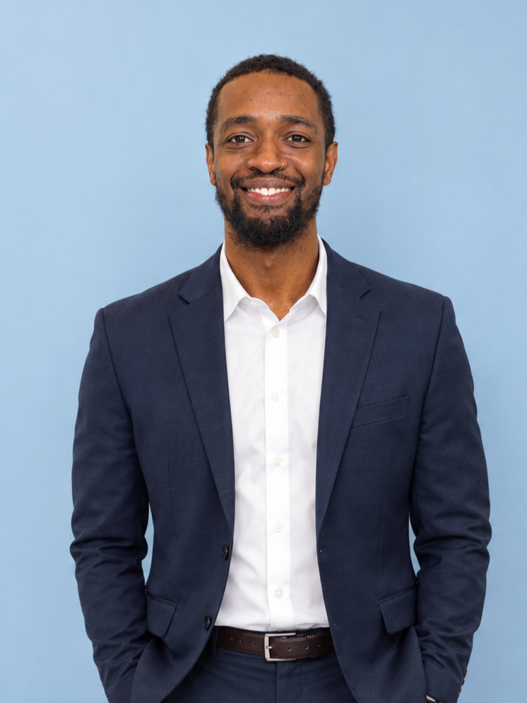 man in navy suit on light blue background smiling