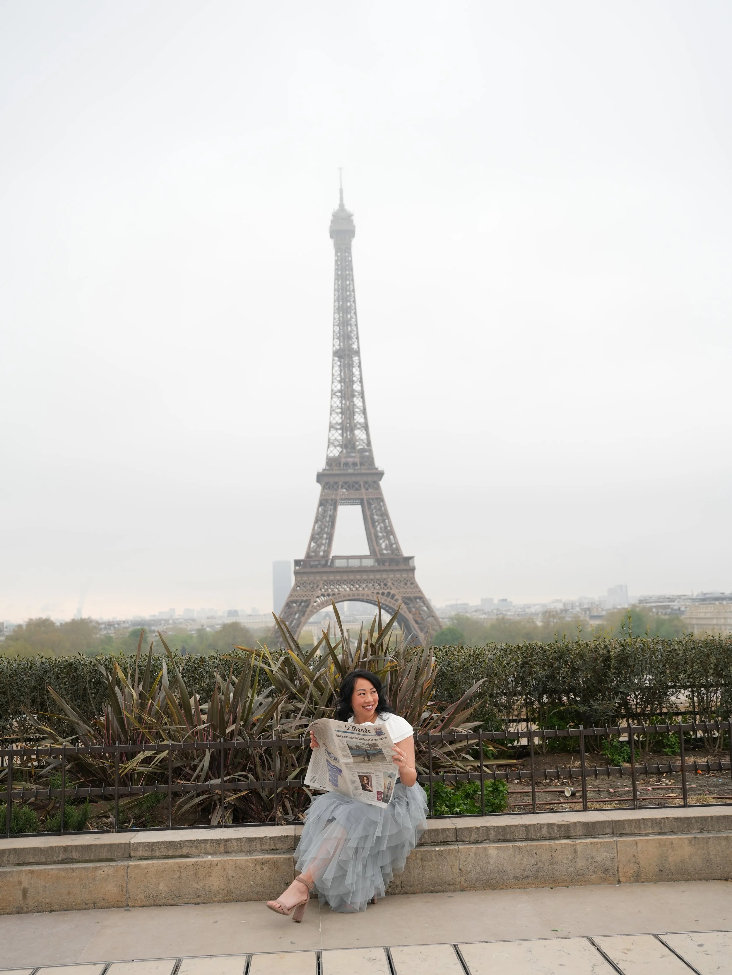 A woman sits on a bench reading a newspaper with the Eiffel Tower in the background, in Paris, France.