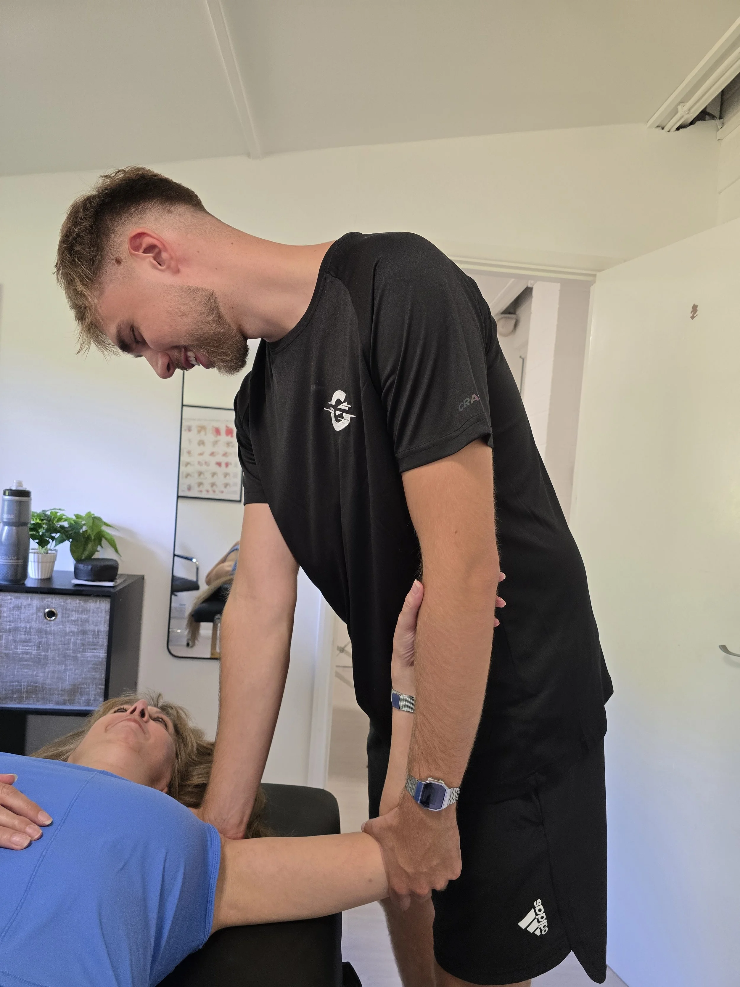 A man providing chiropractic or physical therapy treatment to a woman lying on a therapy table in a clinical setting.
