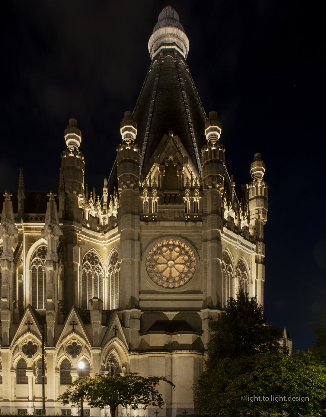 Église éclairée la nuit avec une grande rosace et des détails architecturaux néo-gothiques.
