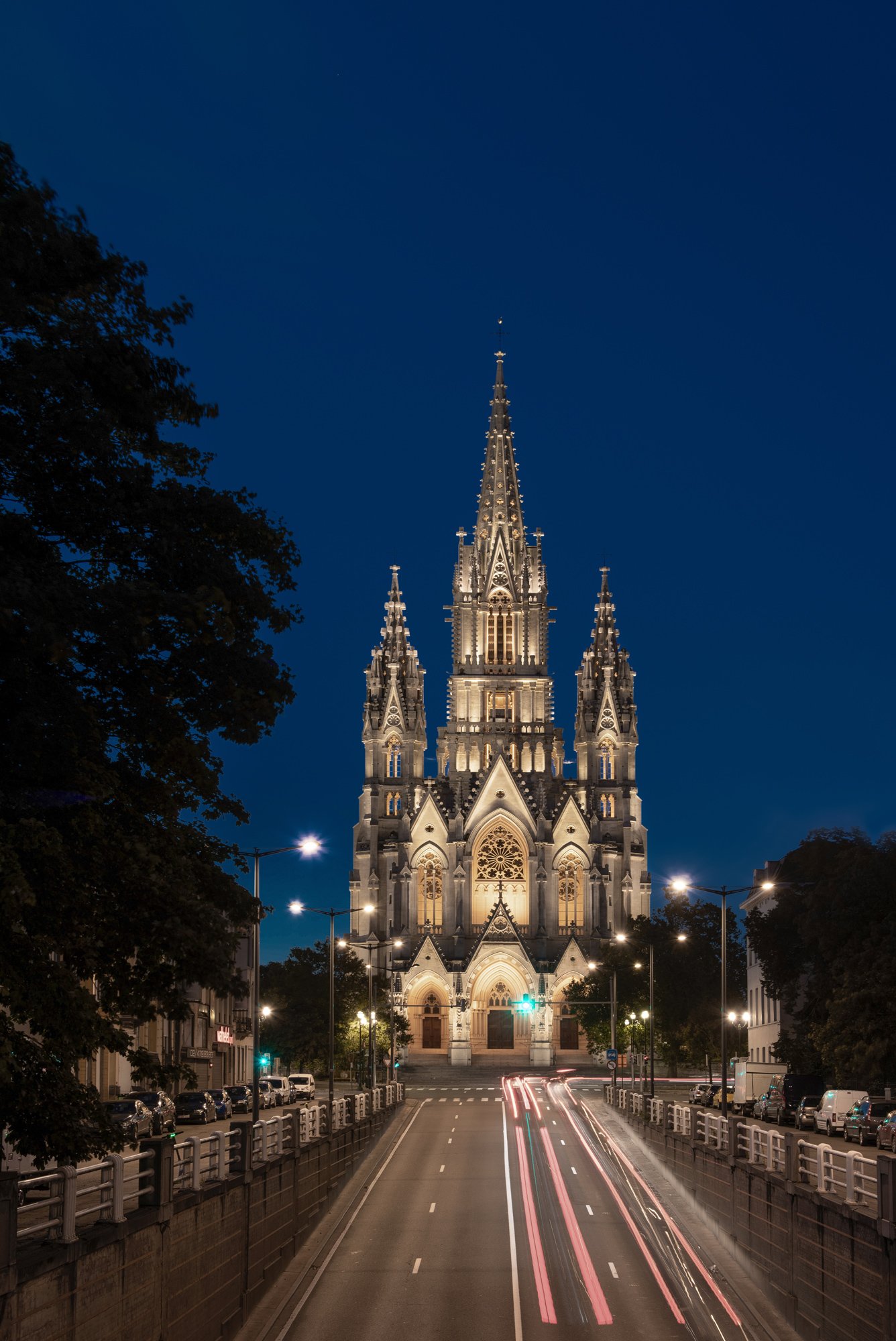 Église néo-gothique éclairée la nuit avec une route au premier plan.