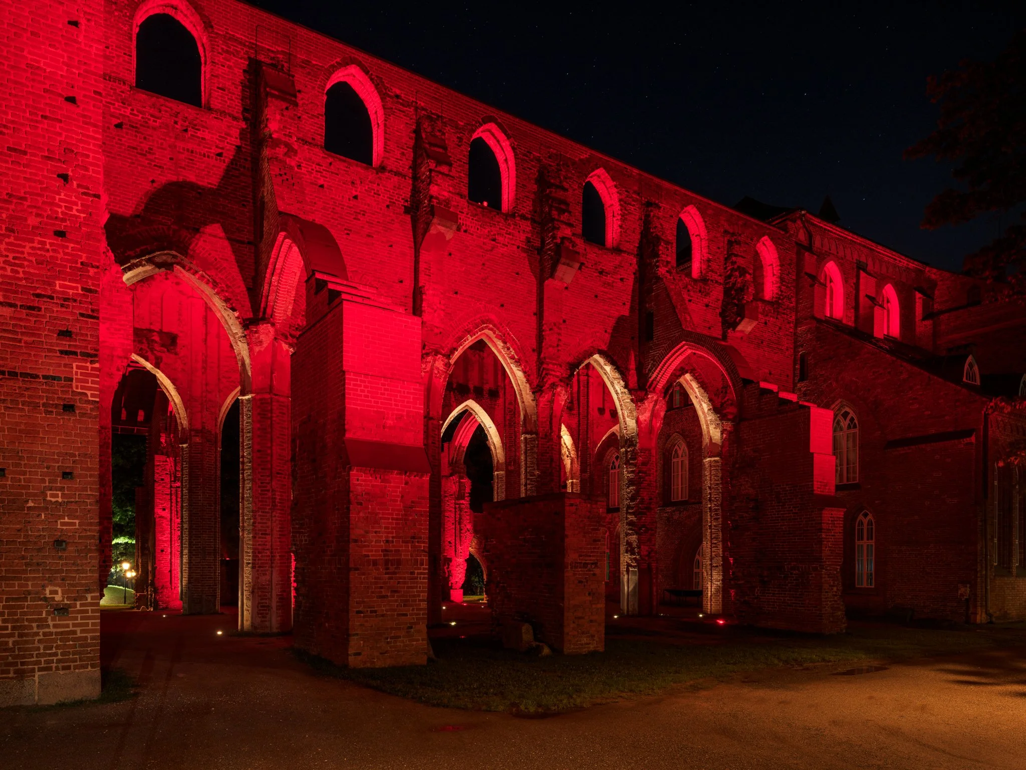 Ruines d'un bâtiment en briques rouges éclairées par des lumières rouges la nuit.