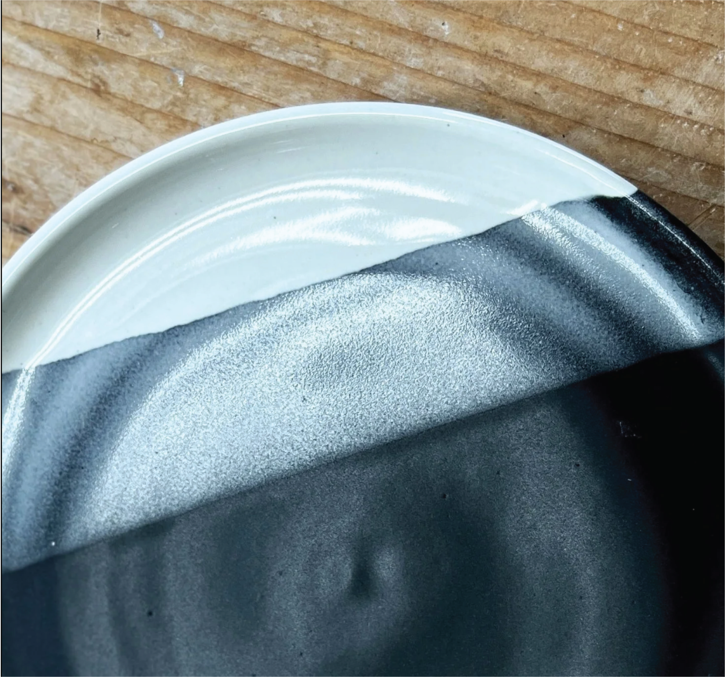 Part of a ceramic mug with a sticker that reads 'sold out' over black paint, on a wooden surface.