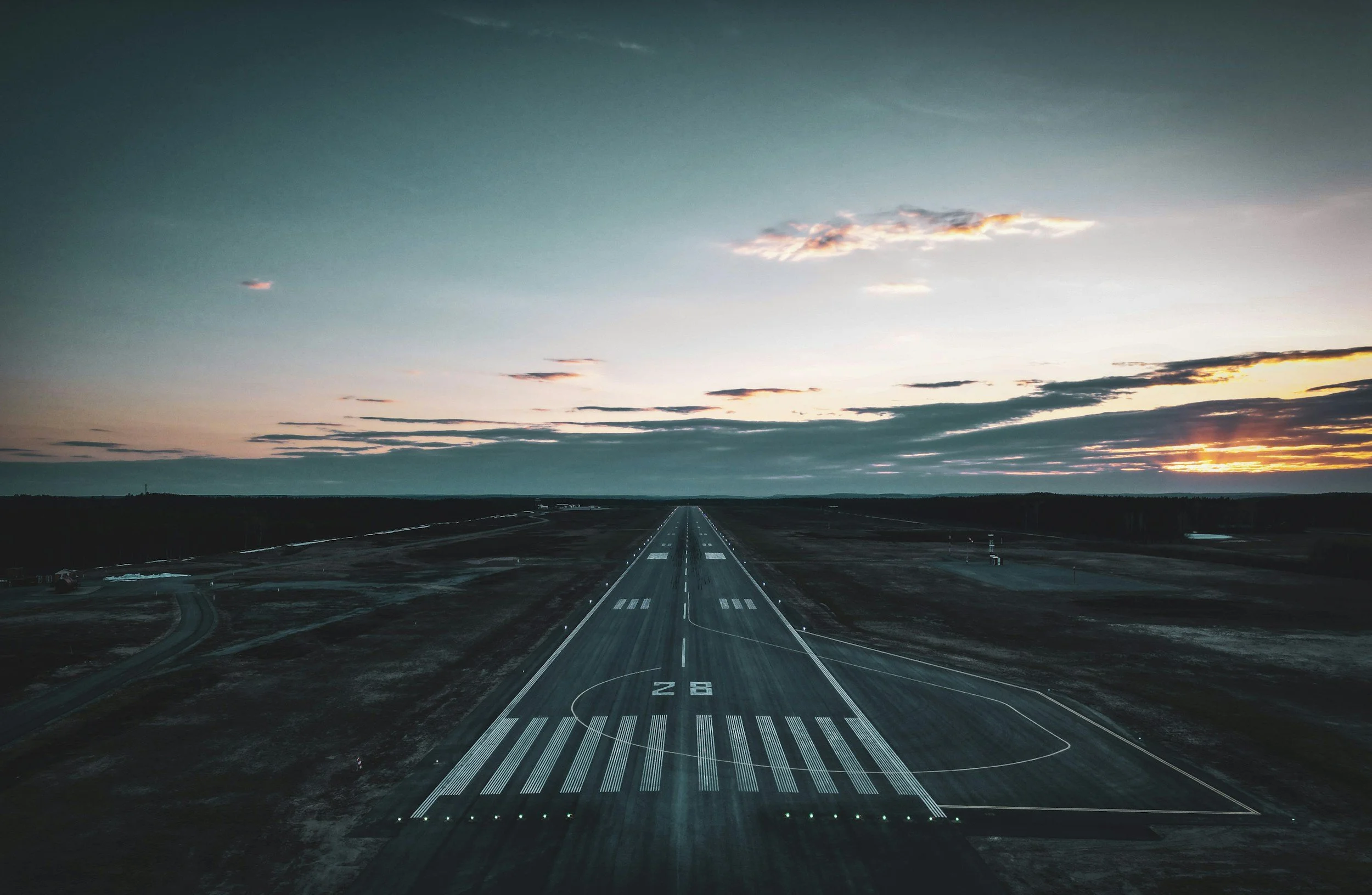 Long runway at an airport during sunset with a cloudy sky.