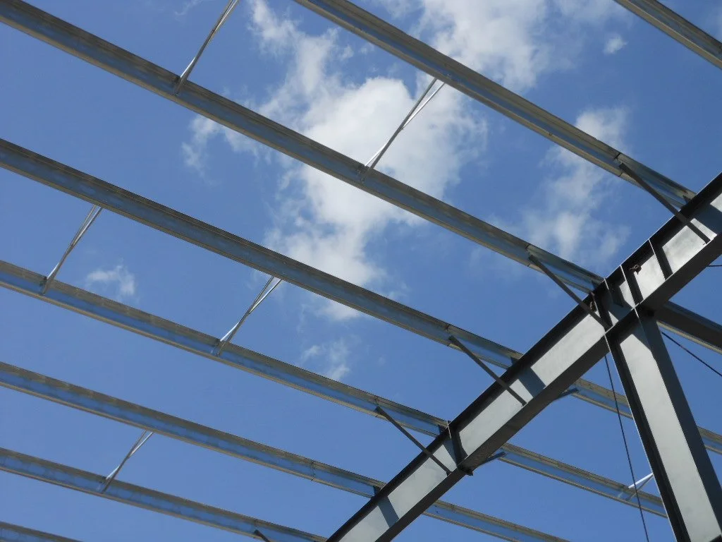 Steel framework of a building under construction against a blue sky with white clouds.