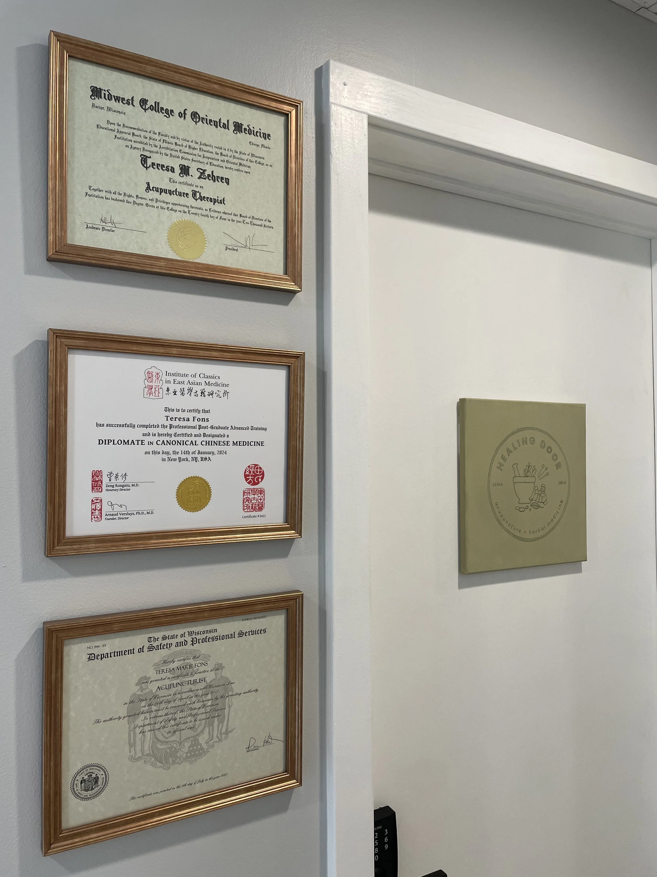 Degrees and license next to treatment room door with Healing Door logo.