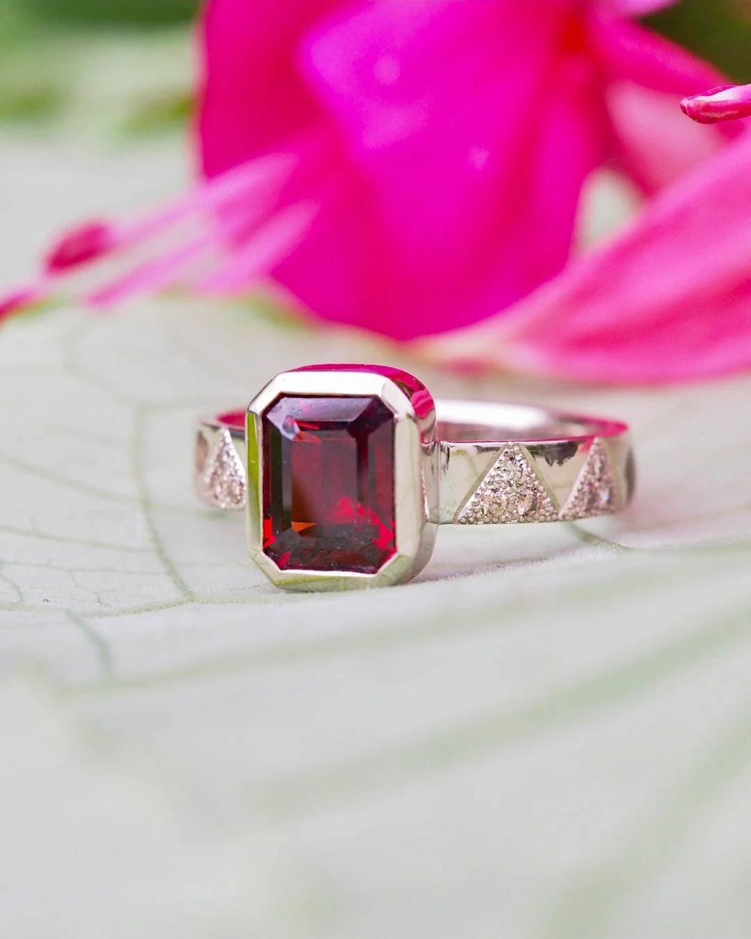Emerald cut garnet ring with diamonds embedded in the platinum band inside of hand-stippled peaks designed to add sparkle, contrast, and interest. There is only one of these rings in the world because it was custom-designed and made for one of our Se