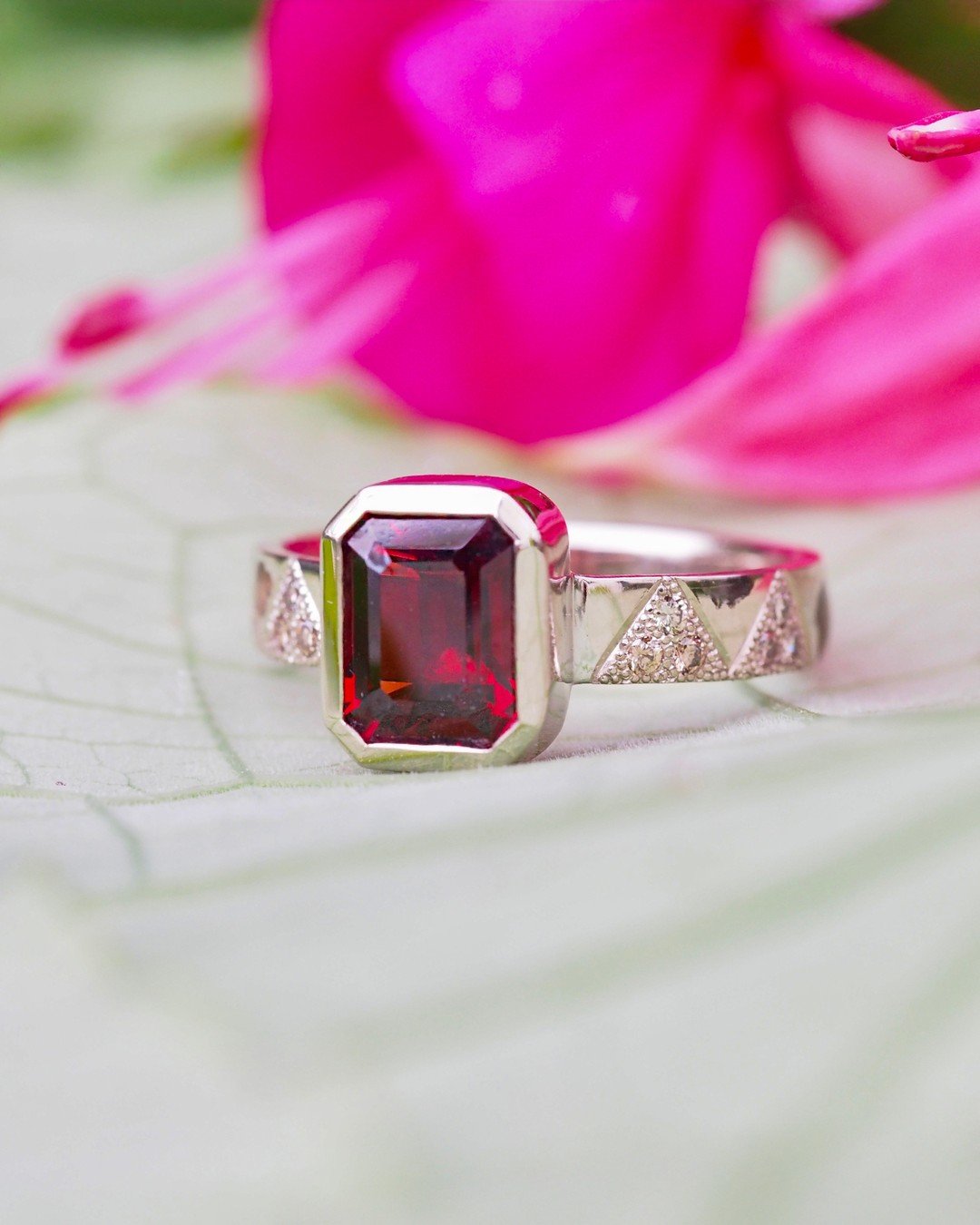 Emerald cut garnet ring with diamonds embedded in the platinum band inside of hand-stippled peaks designed to add sparkle, contrast, and interest. There is only one of these rings in the world because it was custom-designed and made for one of our Se