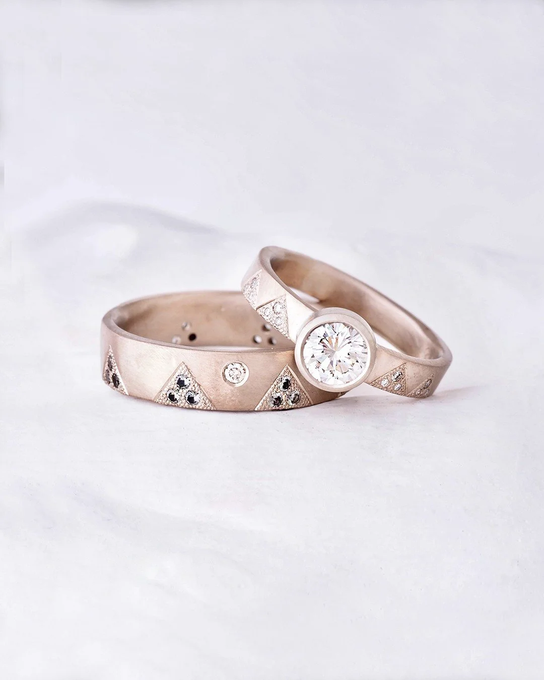 One-of-a-kind wedding ring set designed with mountain peaks that are hand textured and dotted with diamonds in the upper ring and green Montana sapphires in the bottom ring. The larger stones are ethically-sourced white diamonds. Both rings are set i