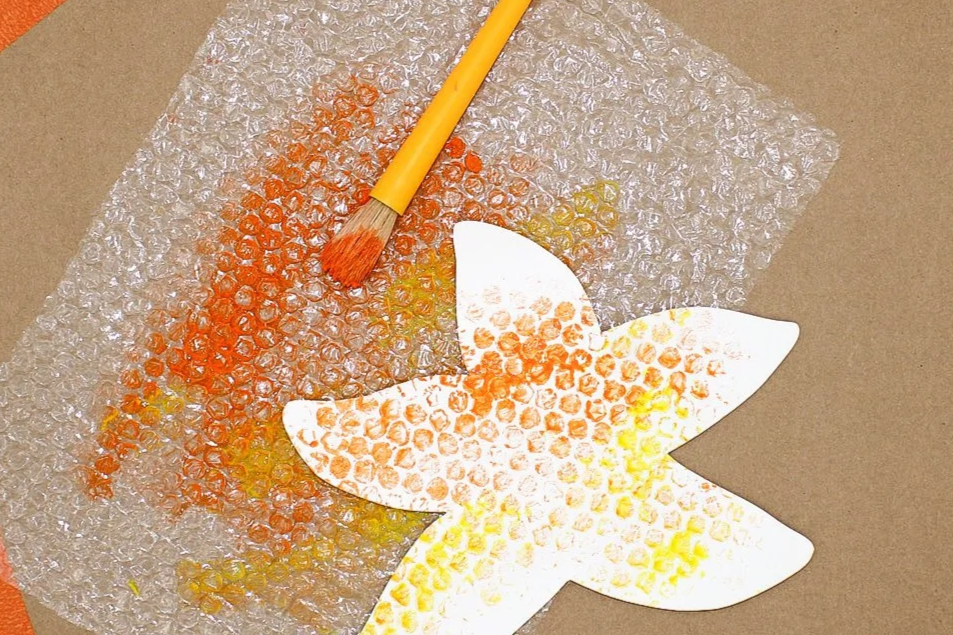 Craft project featuring a paper butterfly with painted spots, a paintbrush, and bubble wrap on a beige surface.
