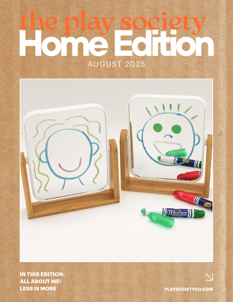 Cover of the August 2025 issue of the Play Society Home Edition magazine, featuring two small whiteboards with childlike drawings of a smiling face and a happy face, surrounded by colorful dry erase markers.