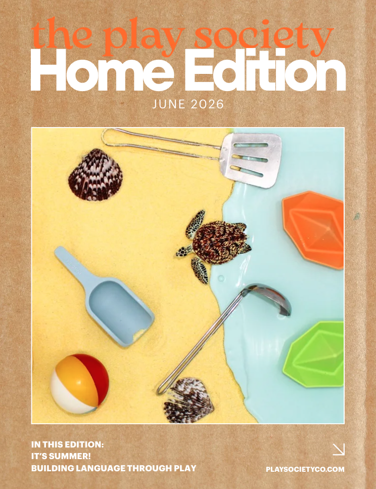 Cover of The Play Society Home Edition magazine for June 2026, featuring a beach-themed scene with seashells, a small plastic shovel, a spatula, a beach ball, and colorful sand molds on a surface that looks like sand and water.