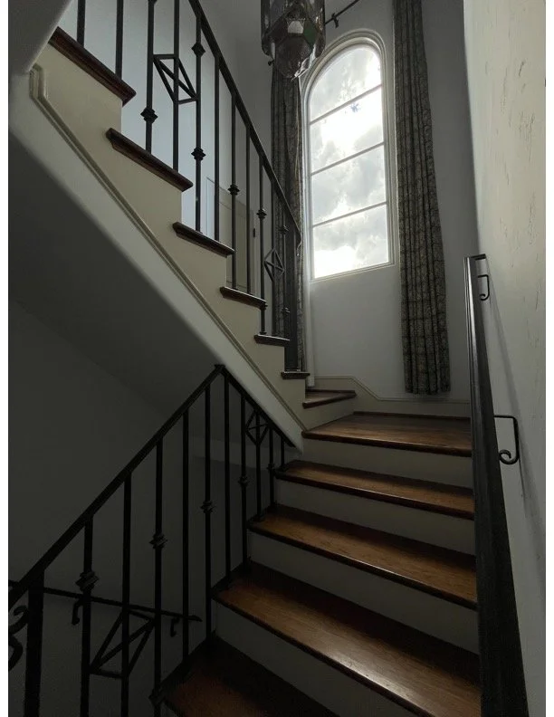Empty living room with gray wooden floors, white walls, large windows, and an open kitchen with wooden cabinets and stainless steel appliances.