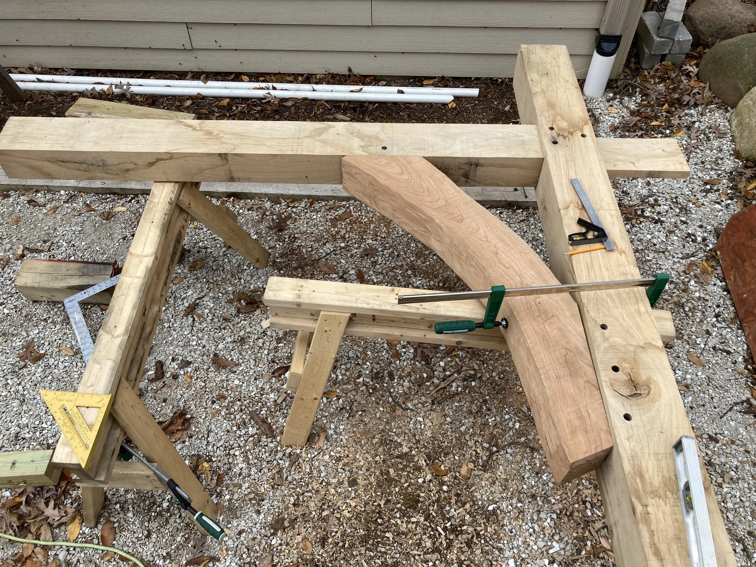 Woodworking project in progress with various lumber pieces, clamps, a square, a level, and Phillips head screwdriver on outdoor work table.