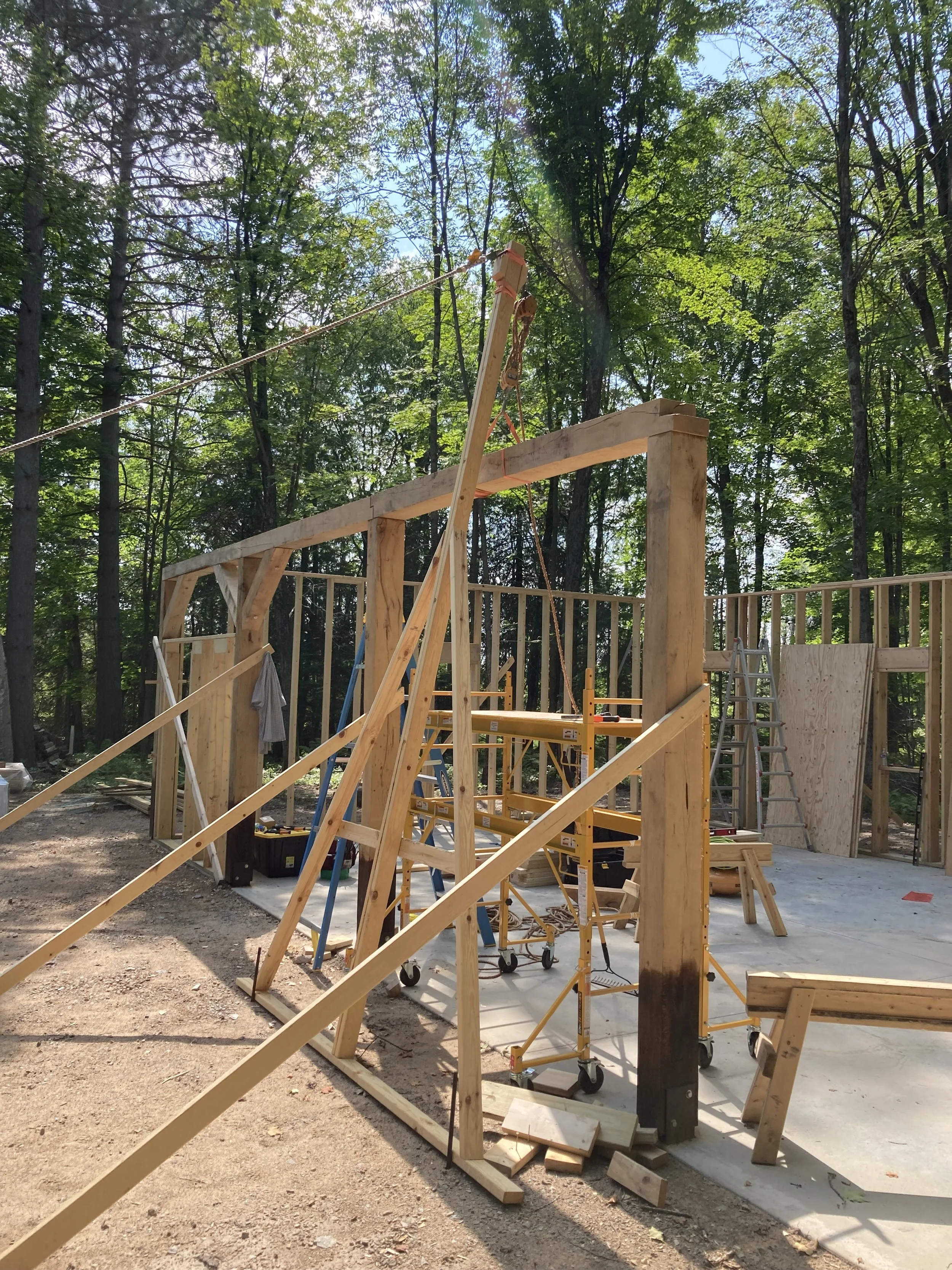 Construction site with wooden framing and scaffolding in progress, surrounded by trees.