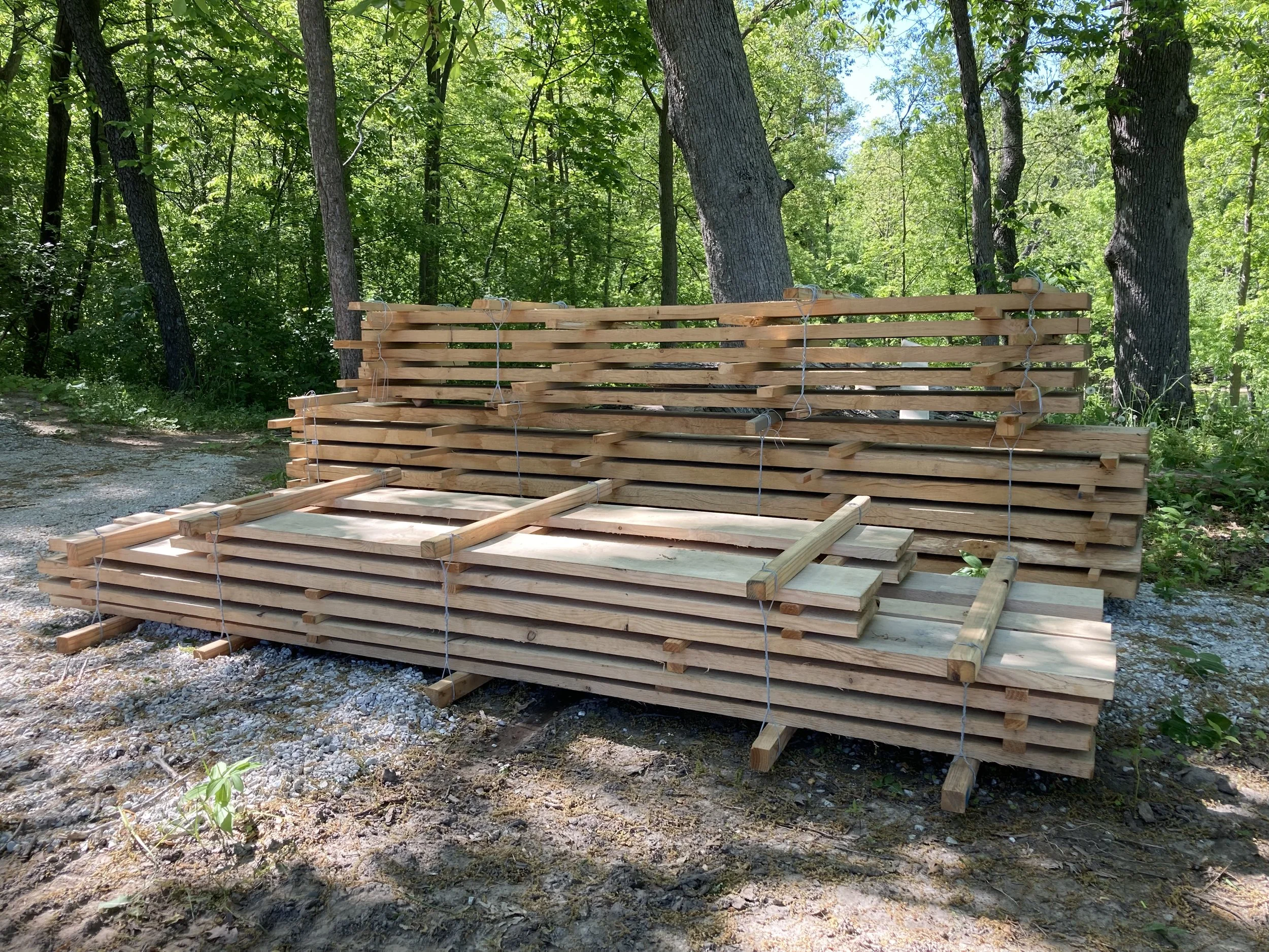 Stacks of wooden pallets with secured strings in a forested outdoor area.