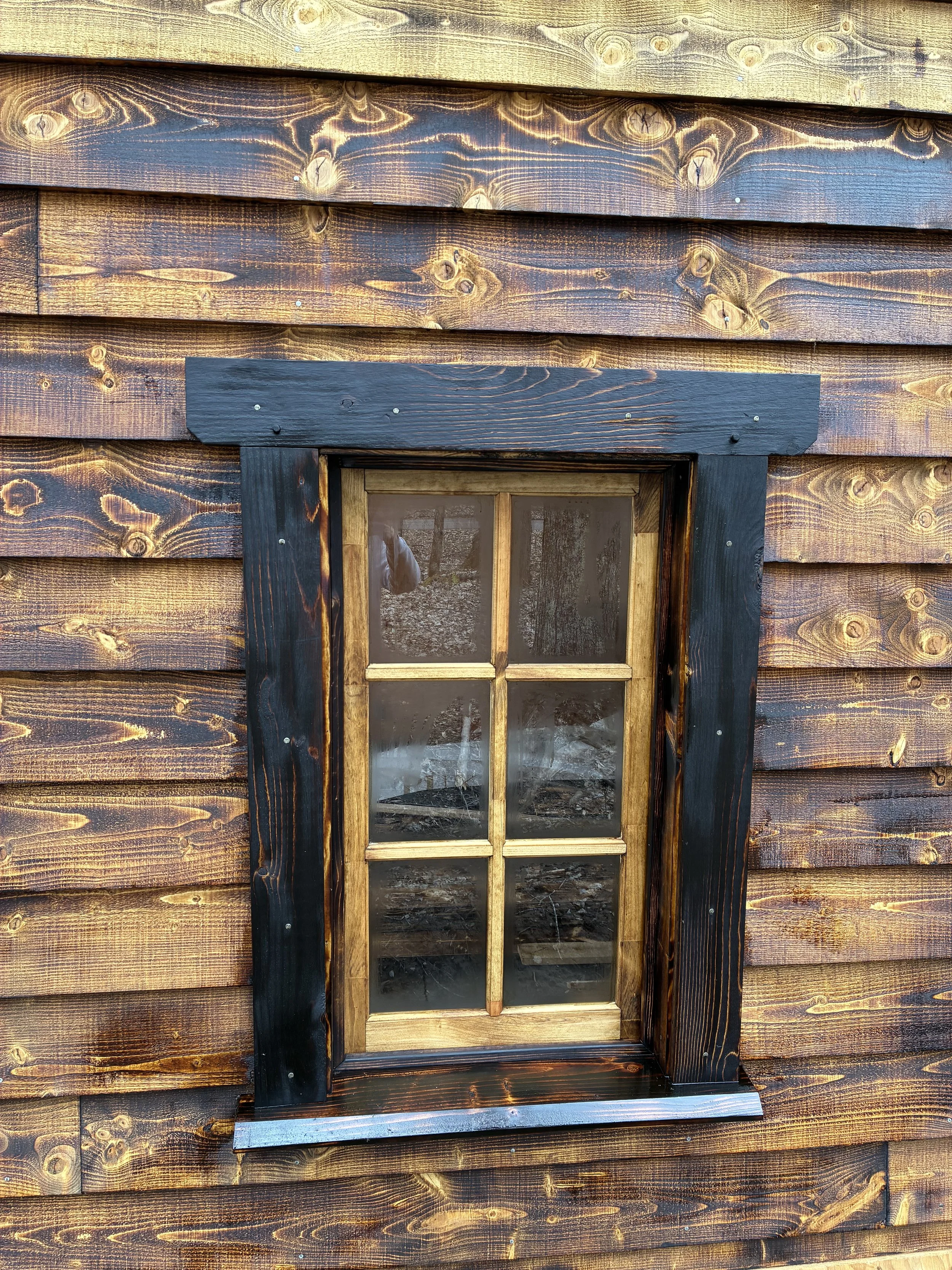 A wooden window with a black-painted frame on a brown wooden wall.