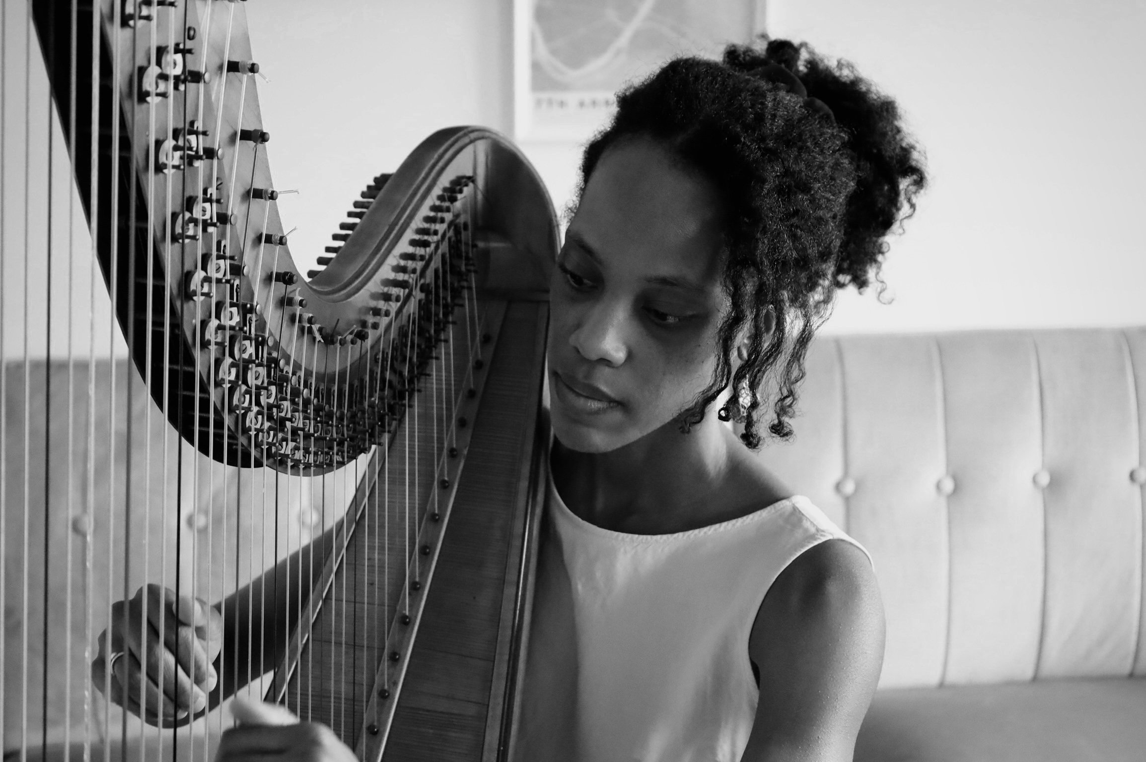 A woman playing a harp, viewed from the side in a black and white photo.