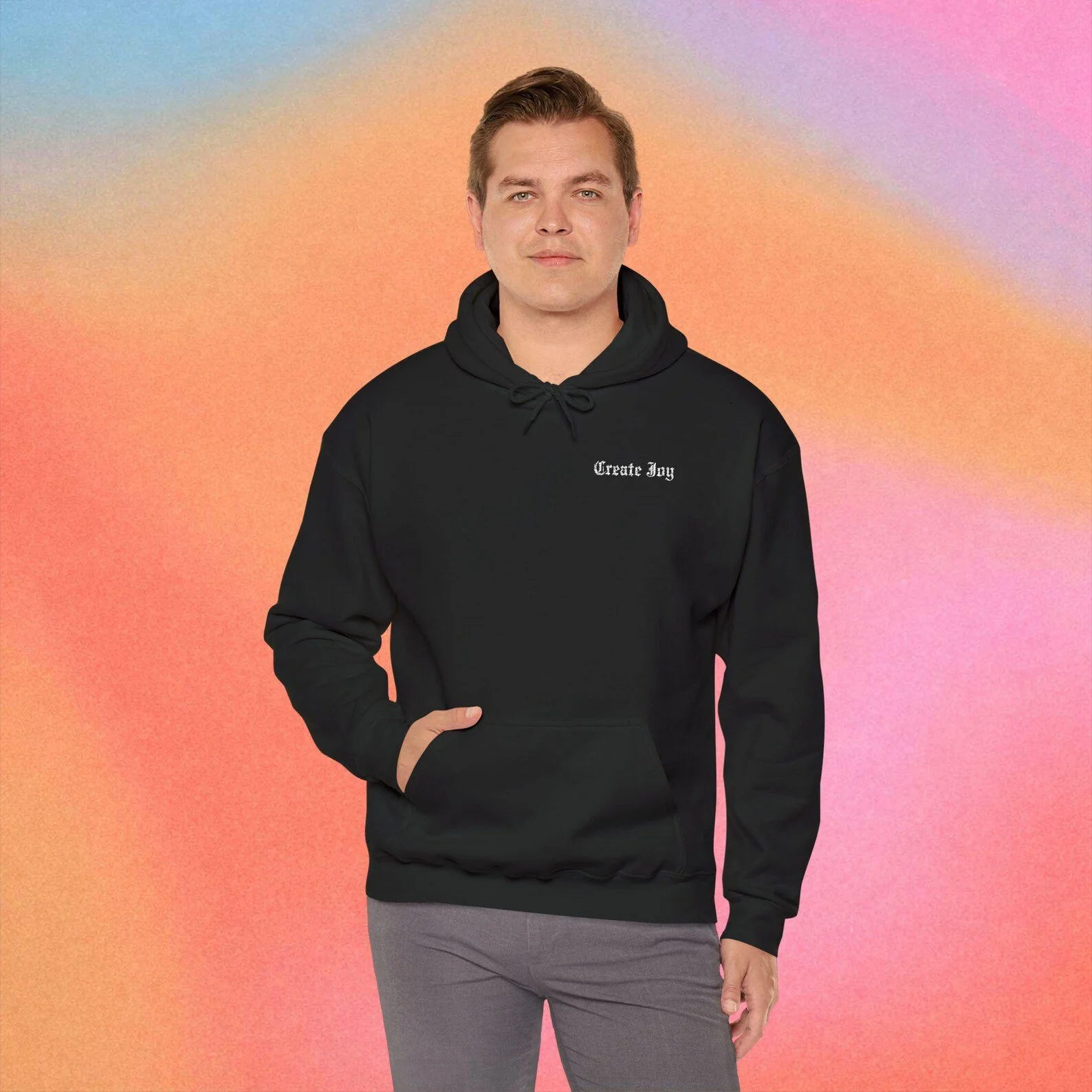 A young man with short brown hair wearing a black hoodie with the words 'Create Joy' written on it, standing in front of a colorful pastel background that transitions from blue to pink and orange.